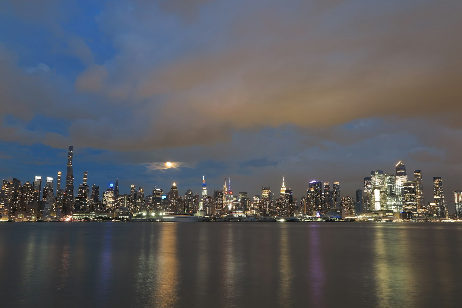 Skyline de la ville la nuit avec des nuages au-dessus et des reflets sur l'eau