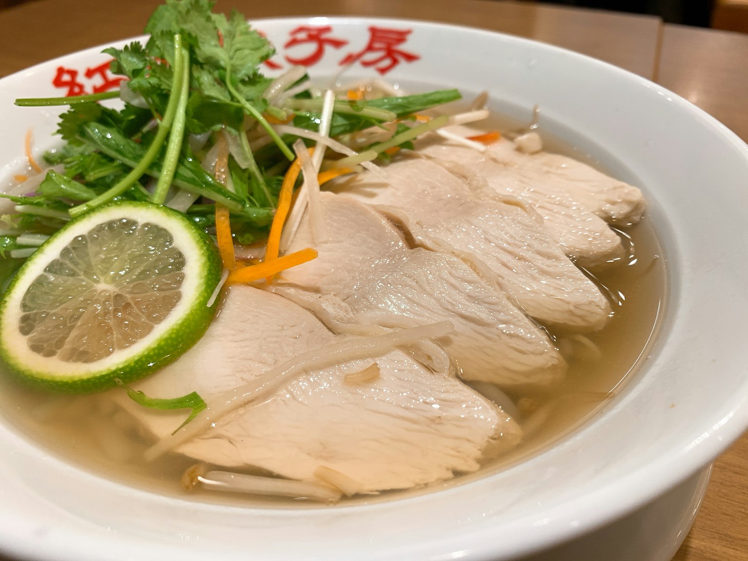ชามซุปไก่ที่มีไก่หั่นบางและสมุนไพรตกแต่งด้วยมะนาว