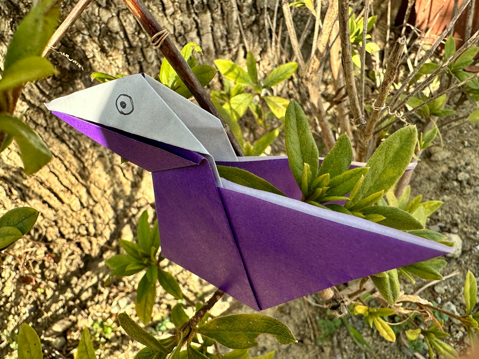 Un uccello di origami viola appollaiato su un ramo di pianta