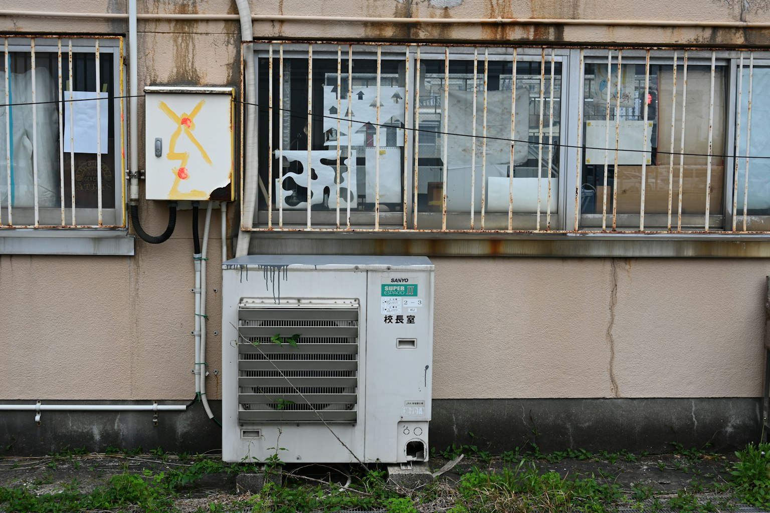 舊建築外牆上的空調和電箱 生鏽的金屬圍欄和雜草叢生的草地