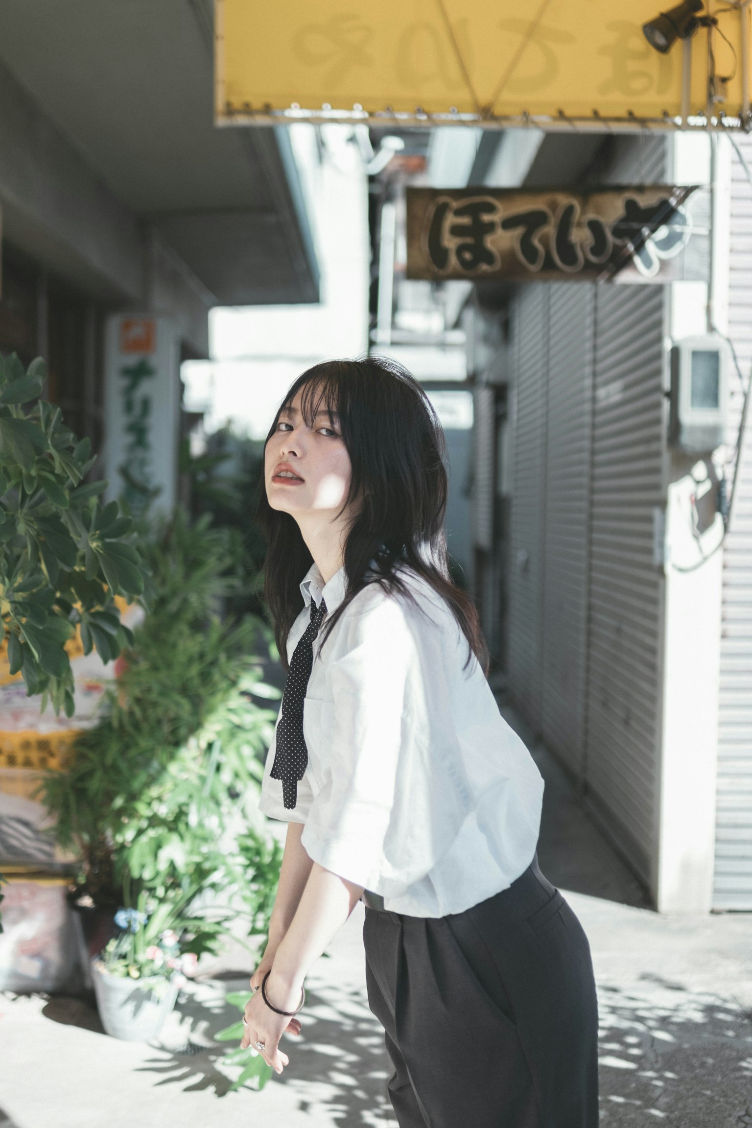 一位女性在街上微笑 穿著白襯衫和黑裙子 附近有植物