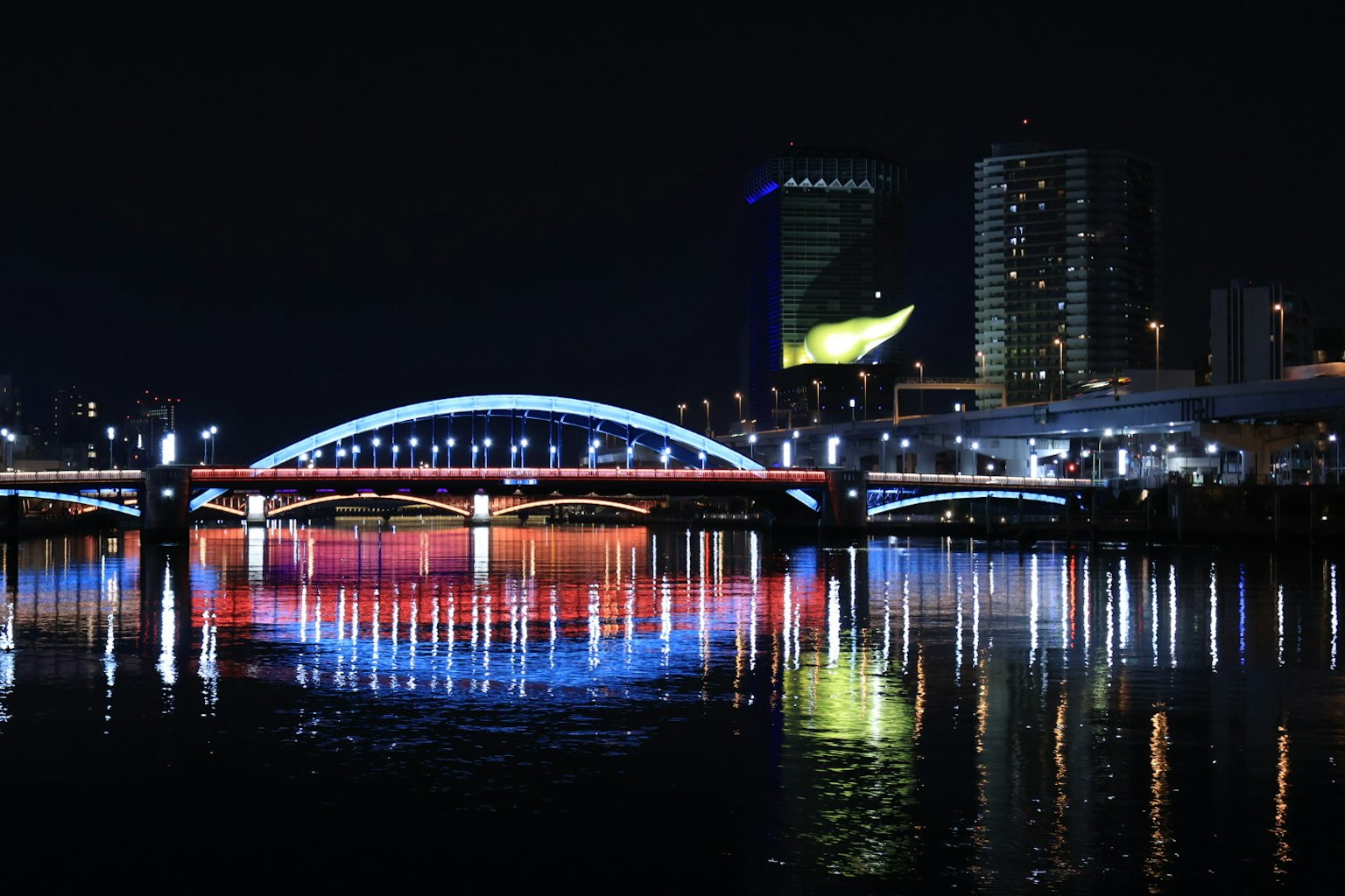 Luci colorate che si riflettono sul fiume con un ponte e edifici di notte