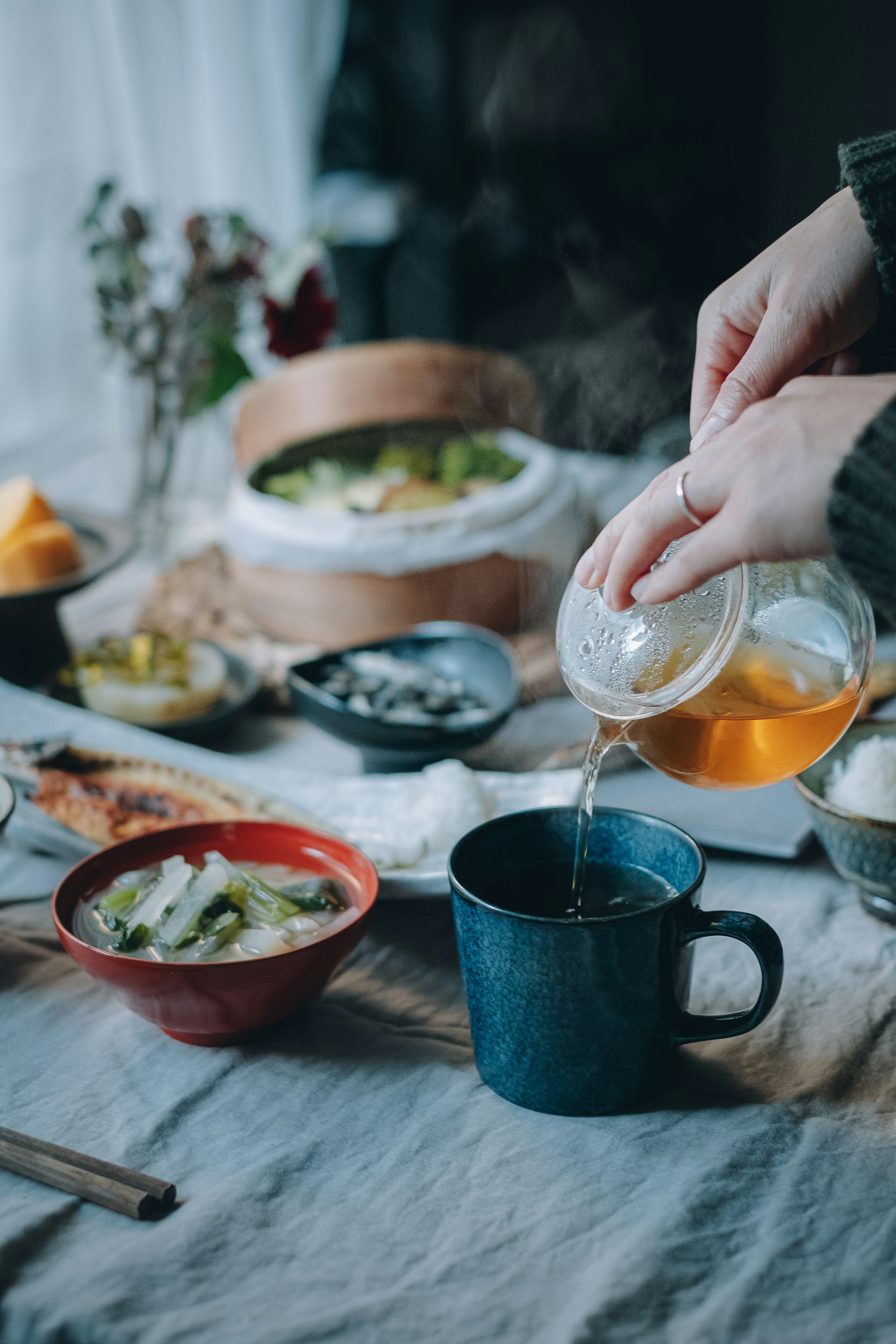 手将茶倒入蓝色杯中，桌上摆放着各种菜肴