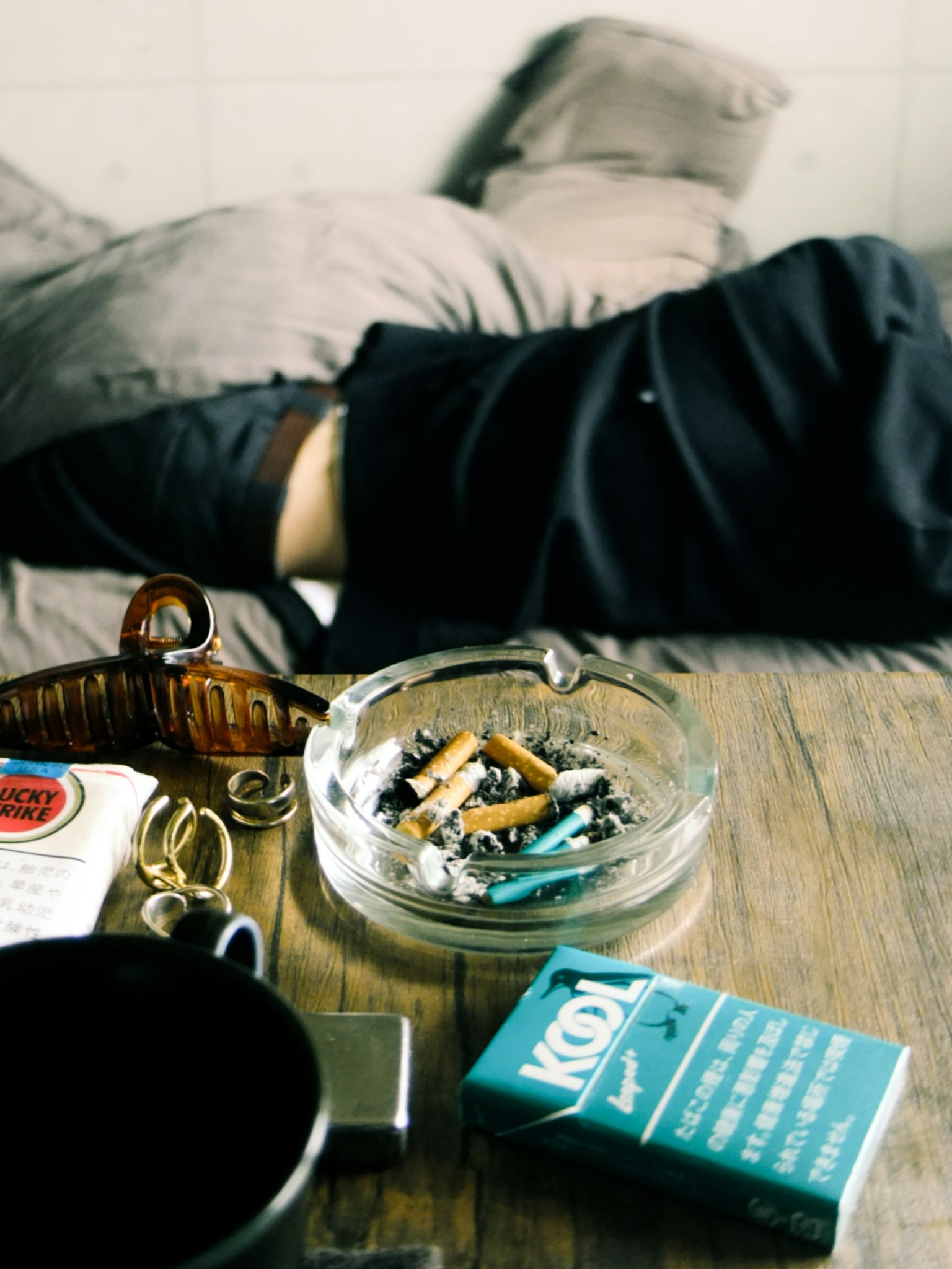 一个人躺在床上，旁边有一个装有烟蒂和各种物品的烟灰缸