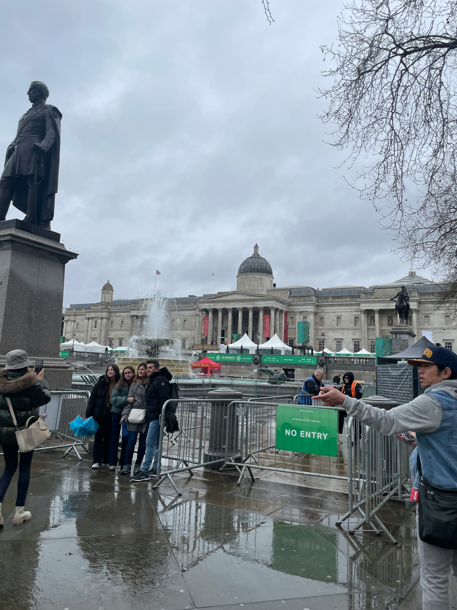 Scena di Trafalgar Square con una statua e persone cielo nuvoloso con pozzanghere