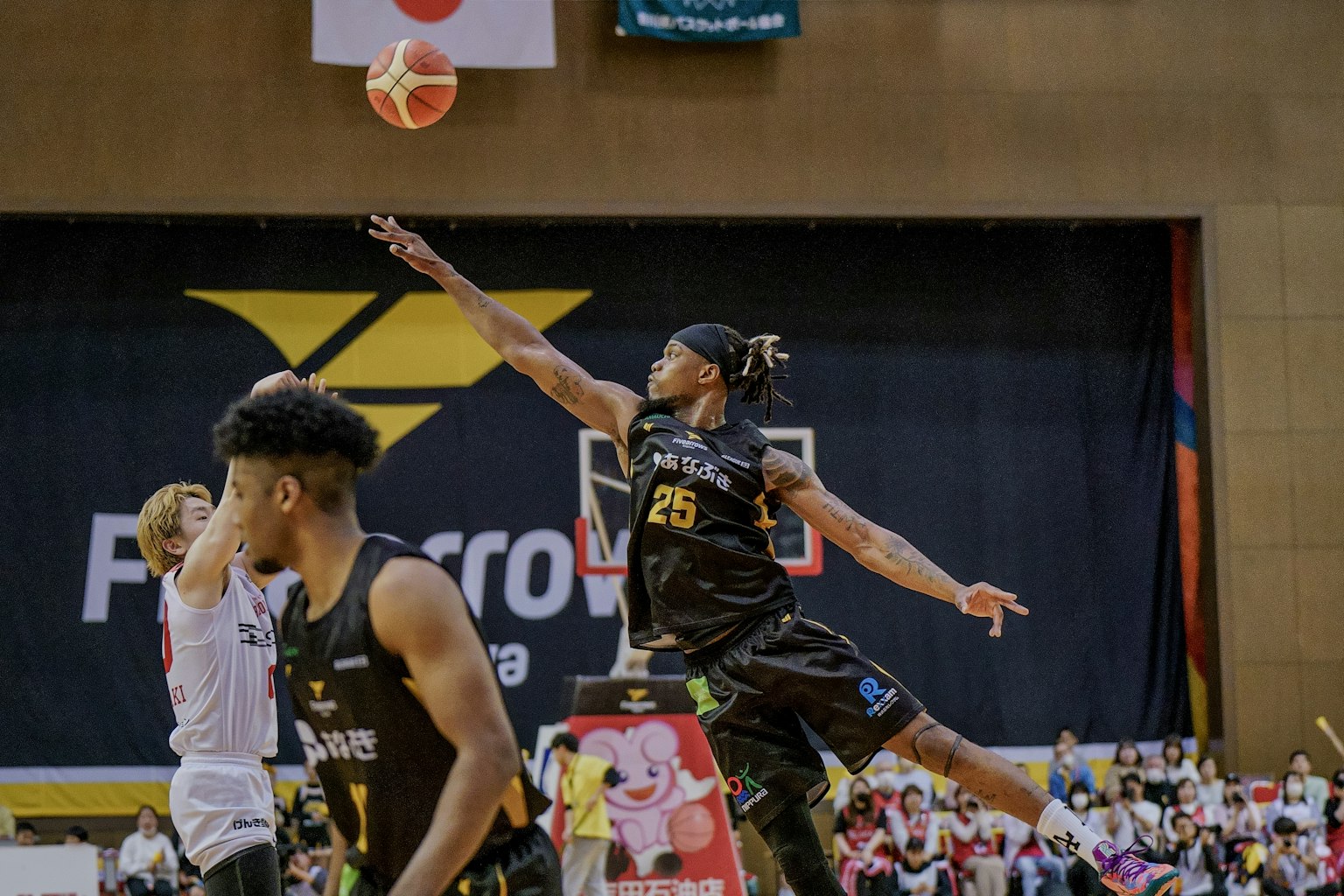 Pemain basket melakukan tembakan selama pertandingan dengan penonton di latar belakang