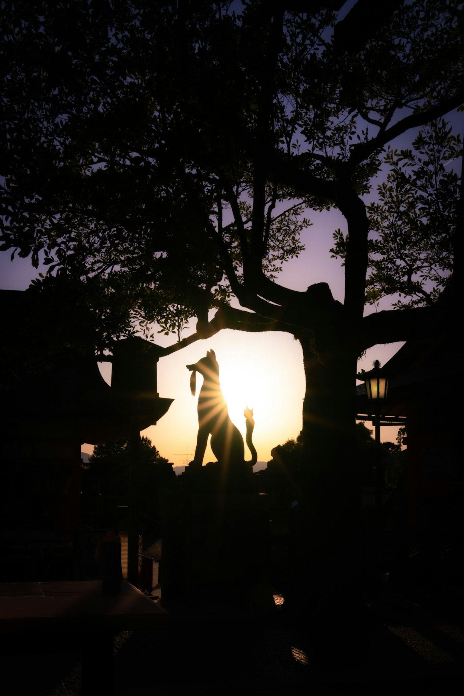Silhouette of a statue and tree against the sunset