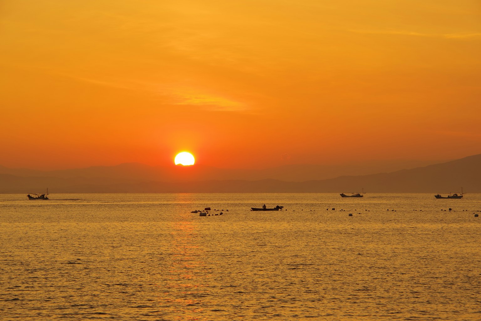 Tramonto sull'oceano con barche su acqua calma