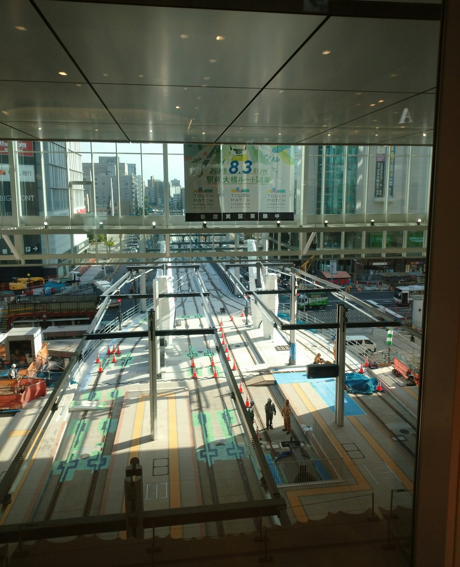 มุมมองของสถานีรถไฟสมัยใหม่ที่มีชานชาลาและรางรถไฟ มีตึกระฟ้าอยู่เบื้องหลัง