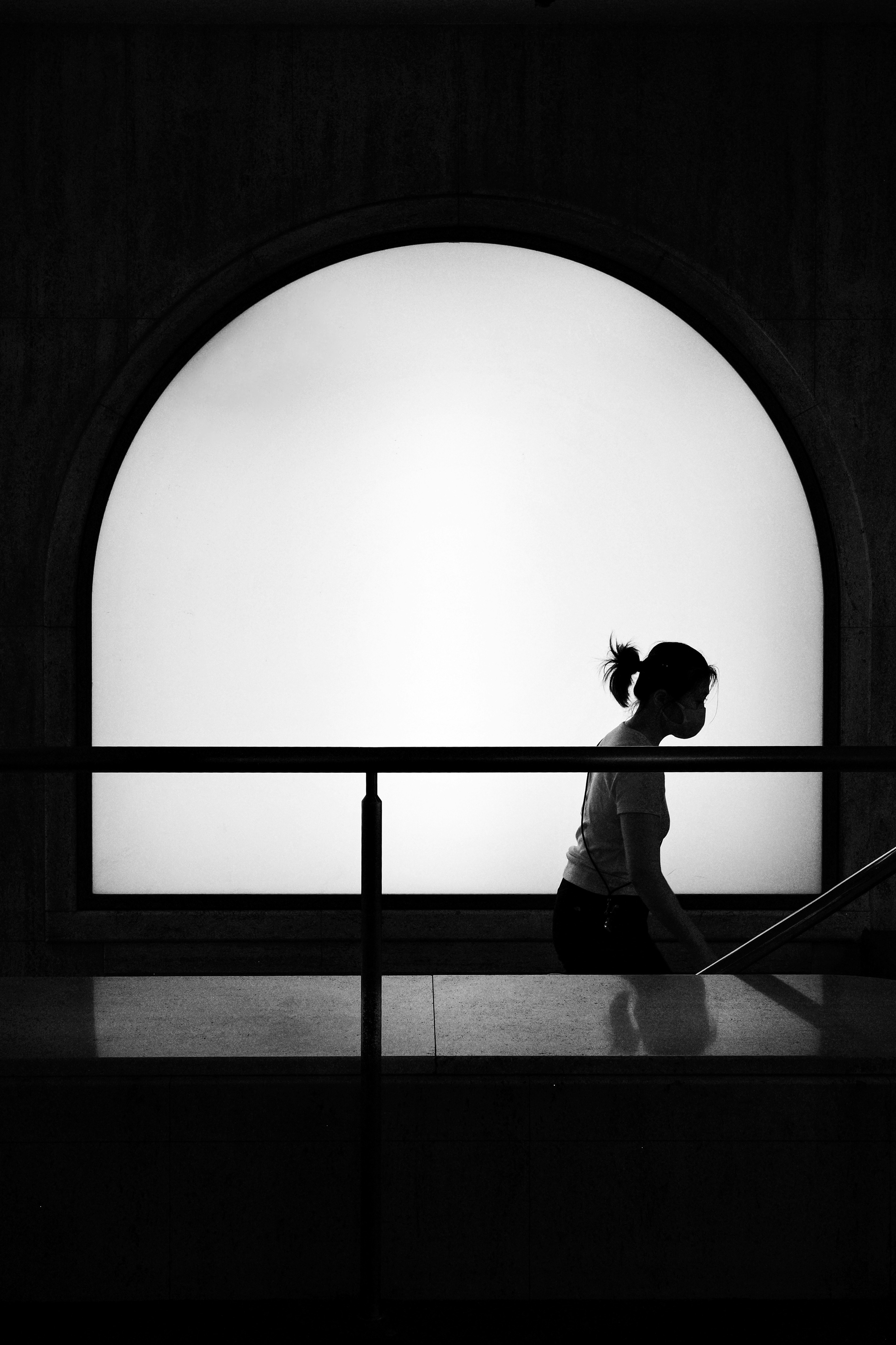 black-and-white silhouette of a person walking in front of an arched window
