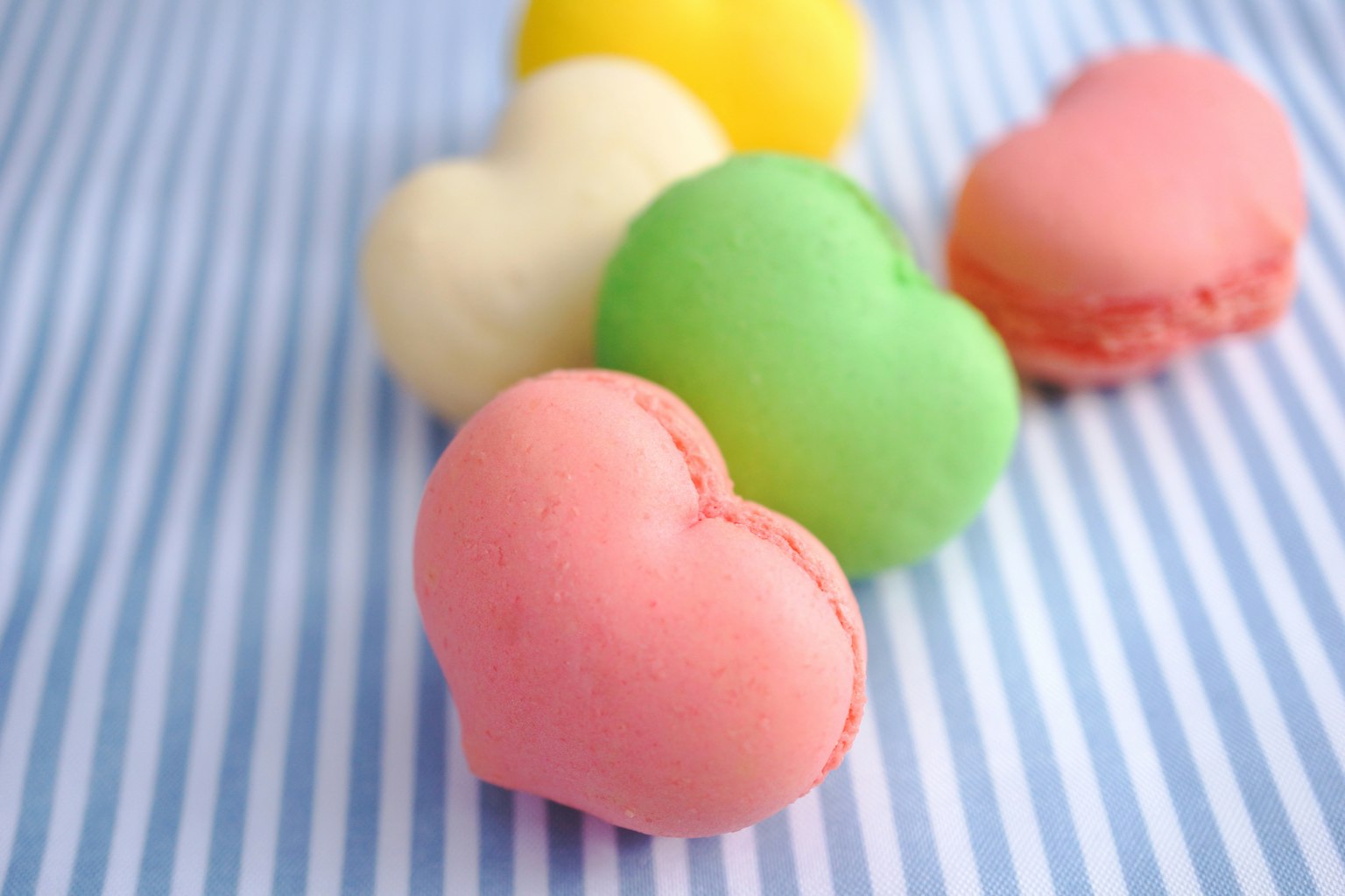 Koleksi macarons berbentuk hati berwarna-warni di atas kain bergaris biru dan putih