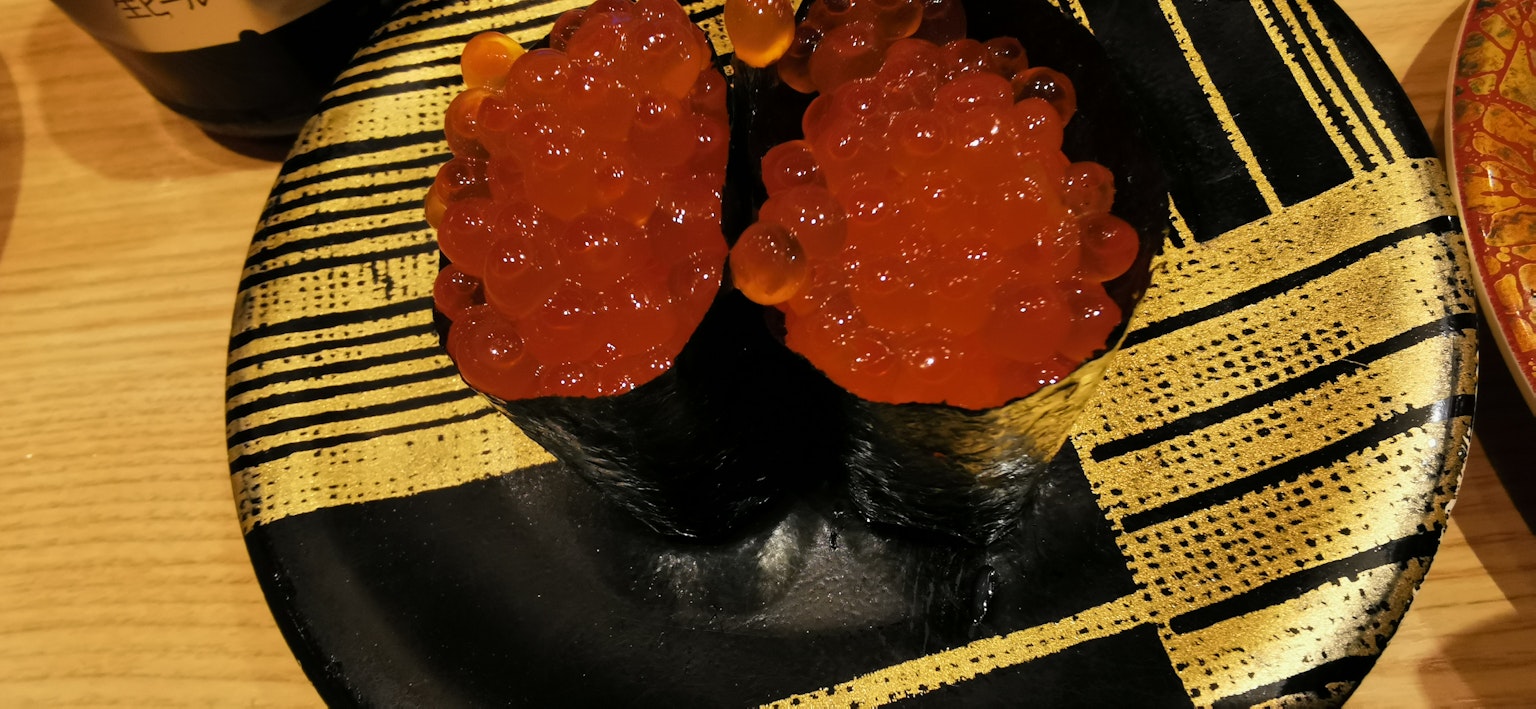 ซูชิอิคุระเสิร์ฟบนจานสีดำที่มีลวดลายตกแต่ง