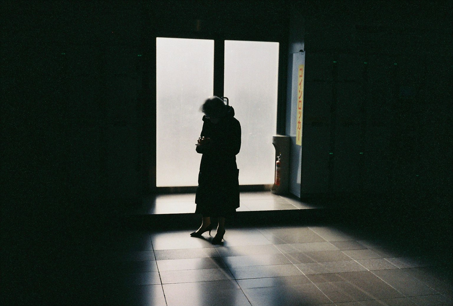 Silhouette of a woman standing in a dimly lit space with a bright window