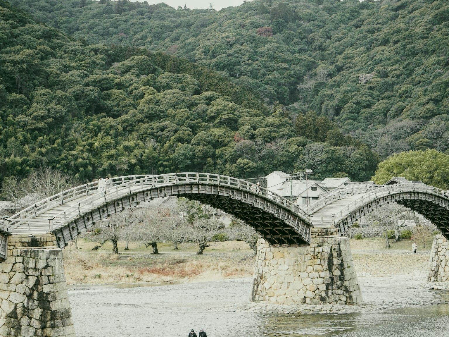 Eine schöne Holzbrücke in Bogenform vor einer grünen Berglandschaft