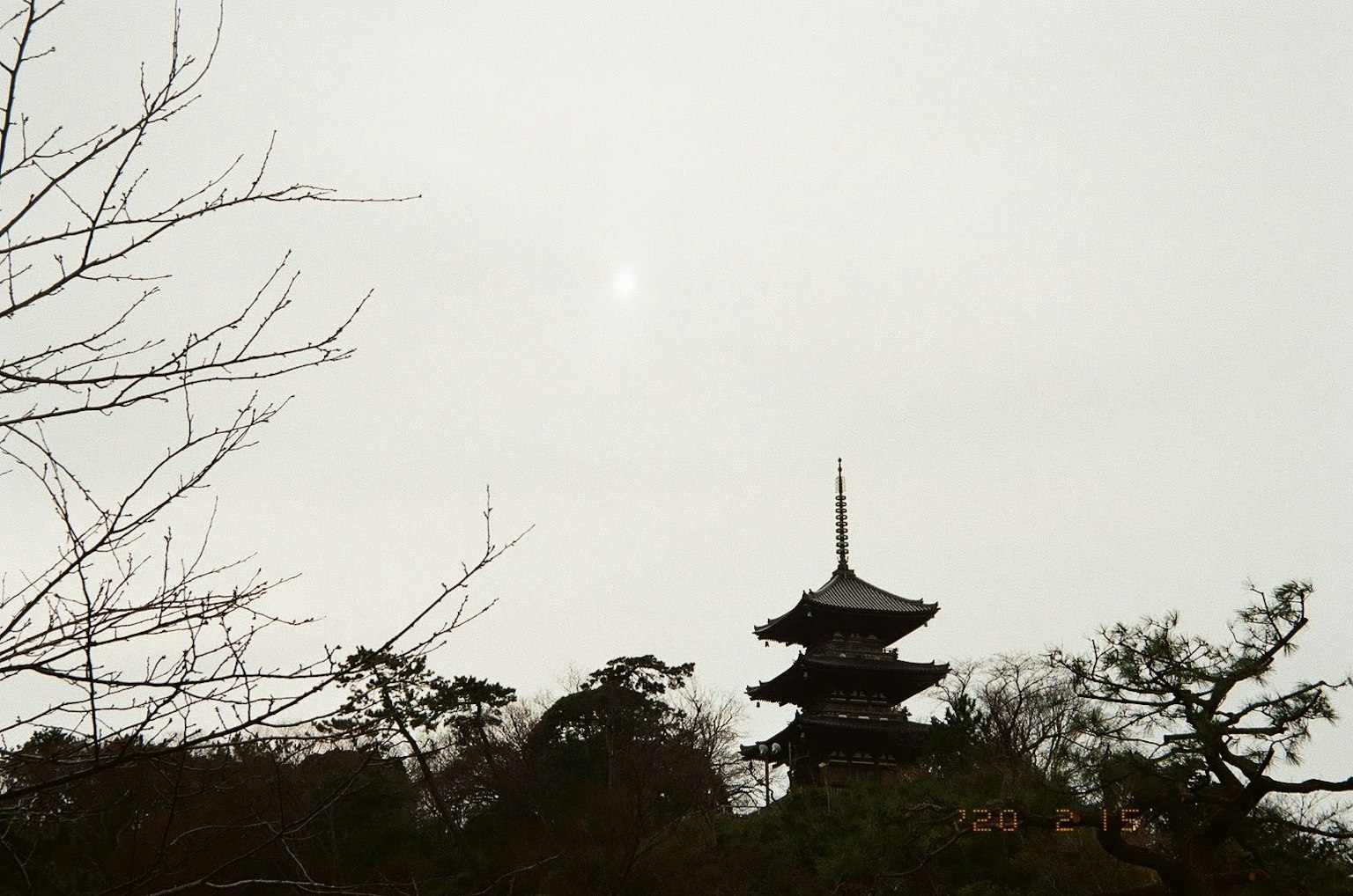 Silhouette of a five-story pagoda against a cloudy sky with trees