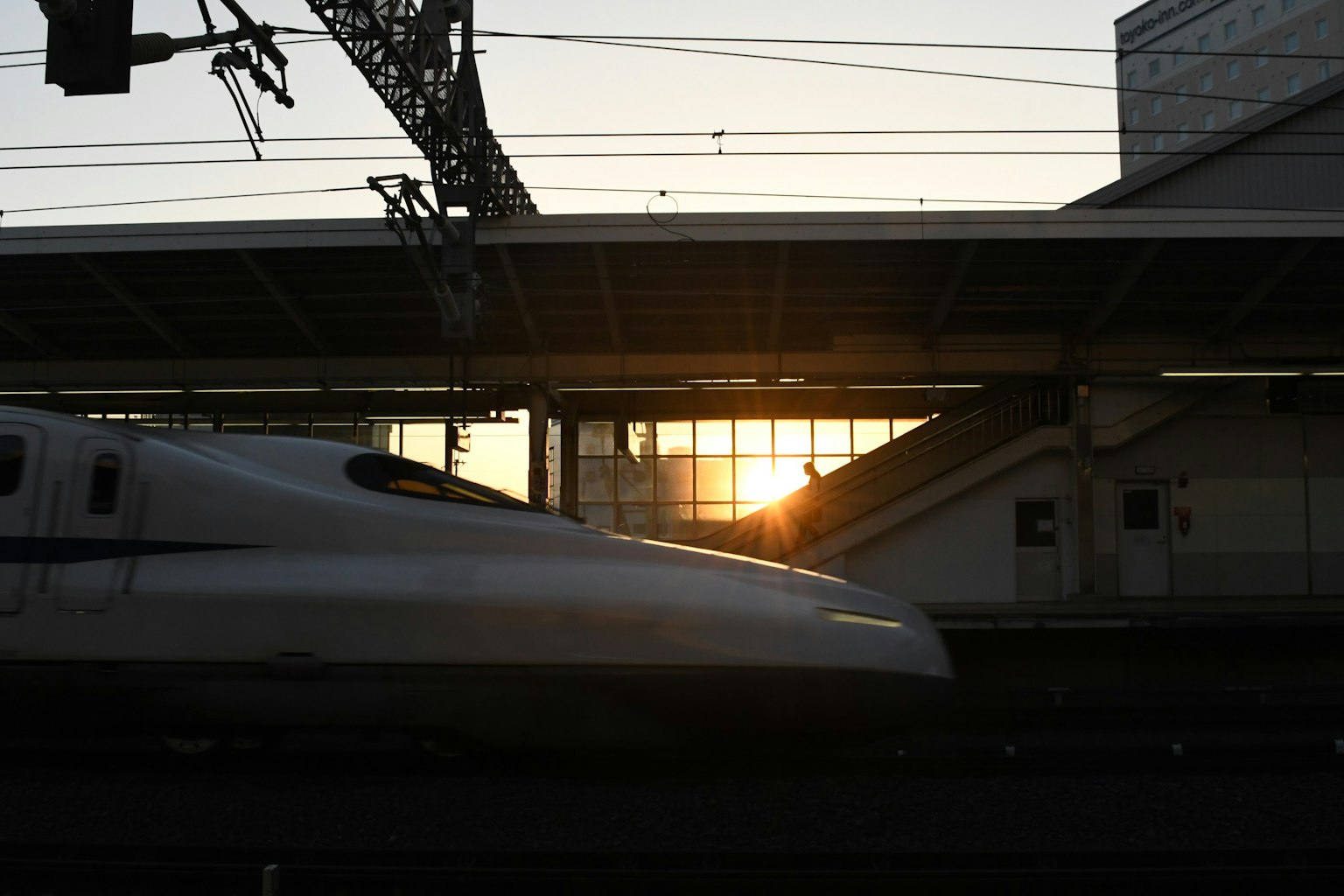 Shinkansen melewati stasiun dengan latar belakang matahari terbenam