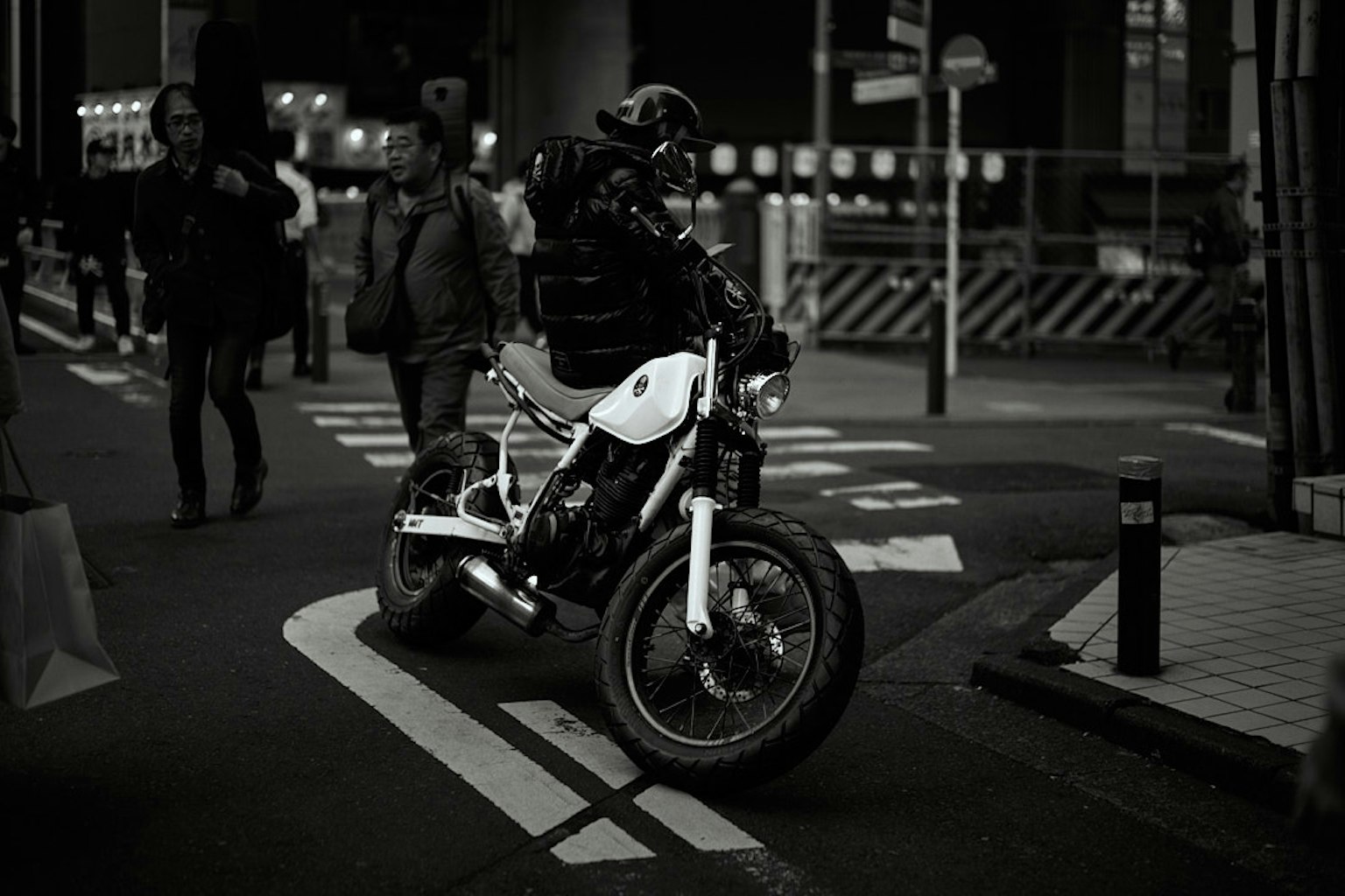 Una scena di strada in bianco e nero con una moto e pedoni