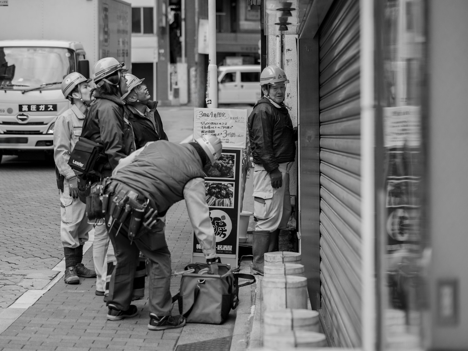 数人の作業員が街の店舗のシャッターの前で作業している様子