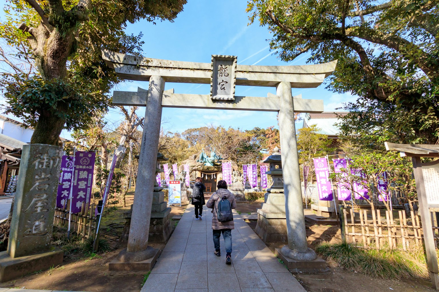 Una persona che cammina sotto un torii in un santuario con lanterne viola sullo sfondo
