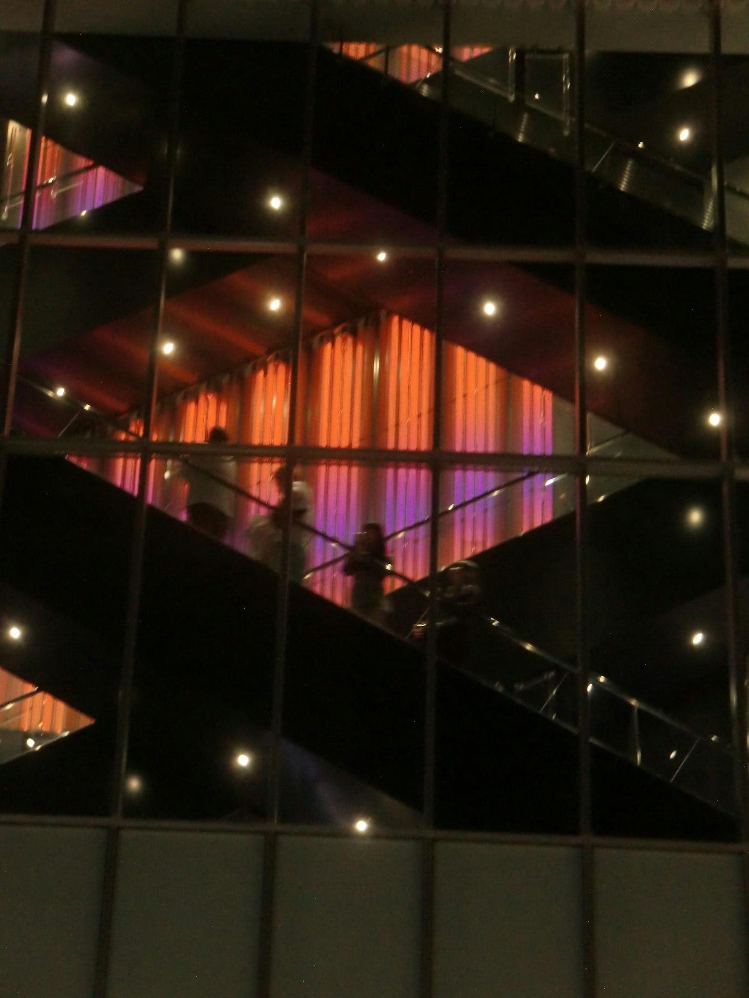 Scala e silhouette di persone viste attraverso una finestra di un edificio di notte con illuminazione arancione e viola brillante