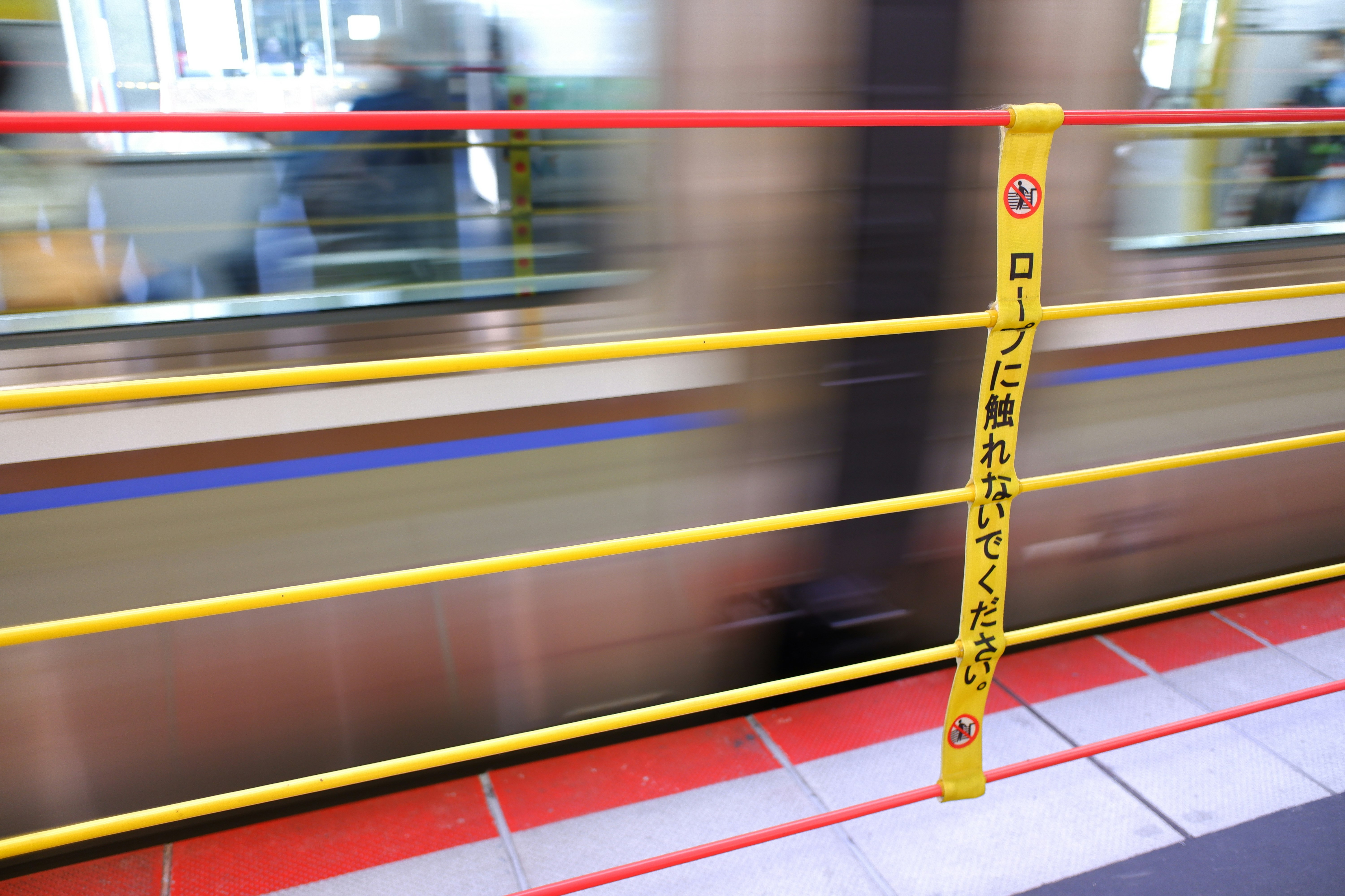 電車の車内で黄色い安全柵と床の床面が見える場面