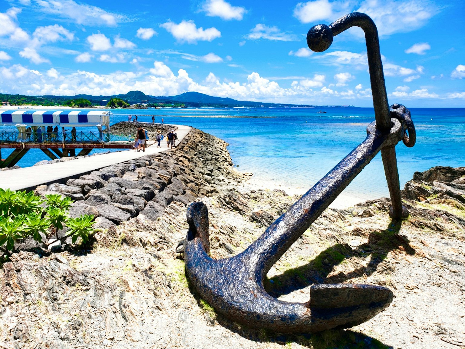 岩石海岸上的大金属锚与清澈的蓝色海洋和天空