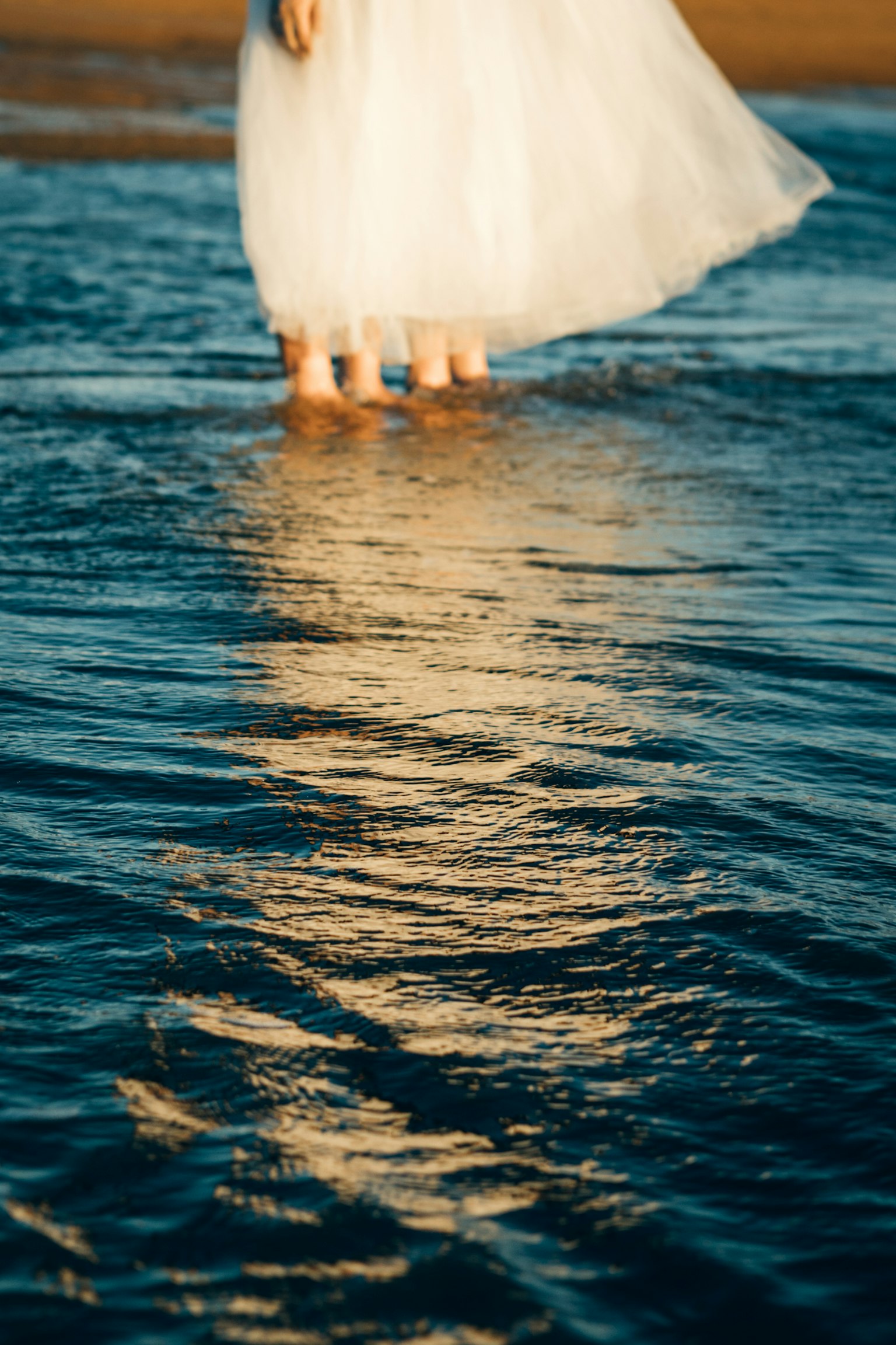 Eine Frau in einem weißen Kleid steht im flachen Wasser mit Reflexionen