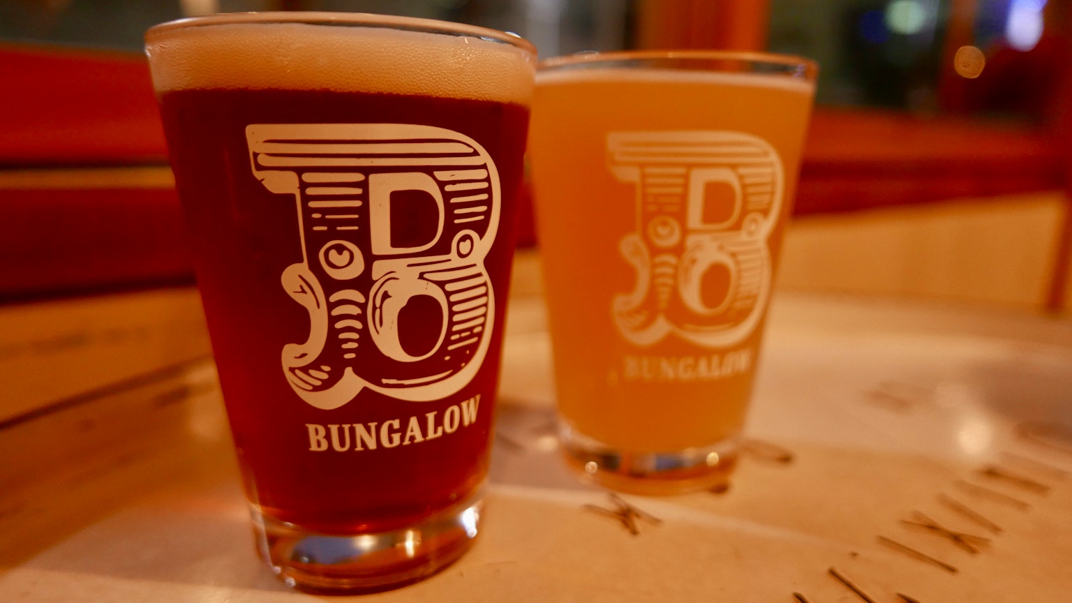 两个啤酒杯并排放置 一个是琥珀色 另一个是浅色 BUNGALOW标志印在上面