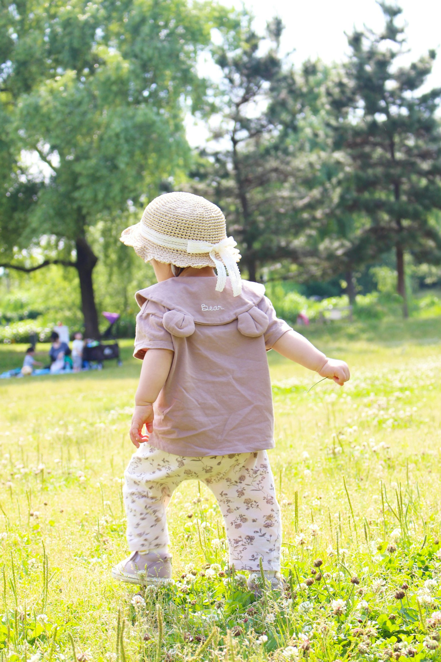 Bambino che cammina in un campo erboso con un cappello e pantaloni floreali