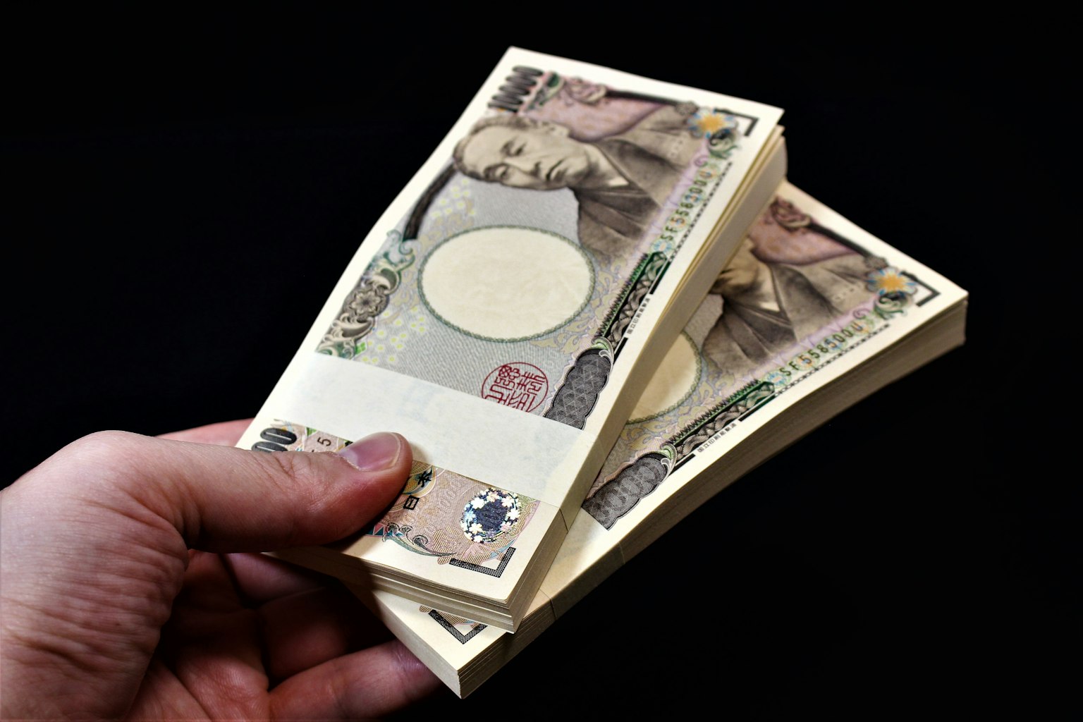 Une main tenant un tas de billets de yen japonais montrant le design de la monnaie