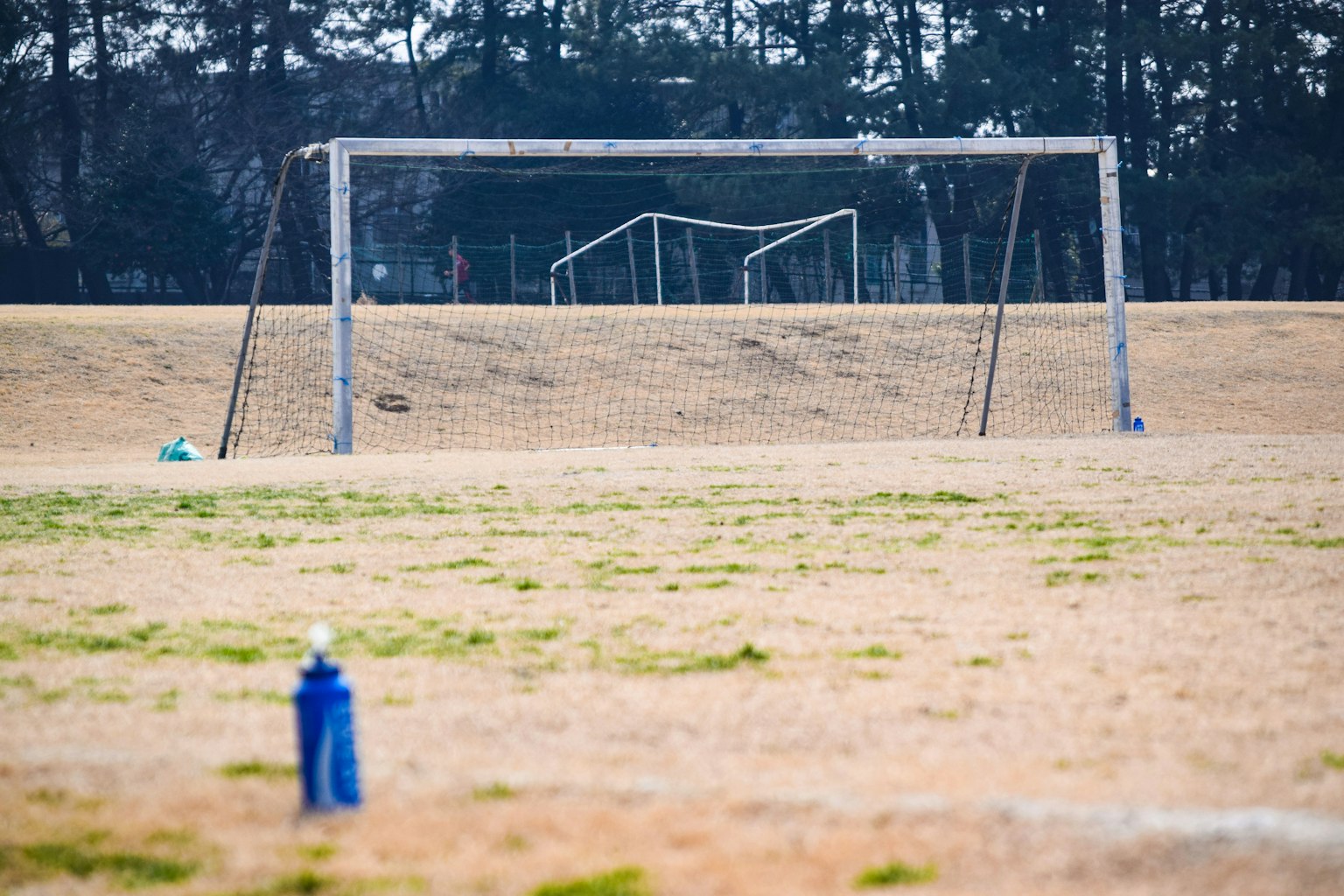 Lapangan luas dengan gawang sepak bola di latar belakang botol air di latar depan