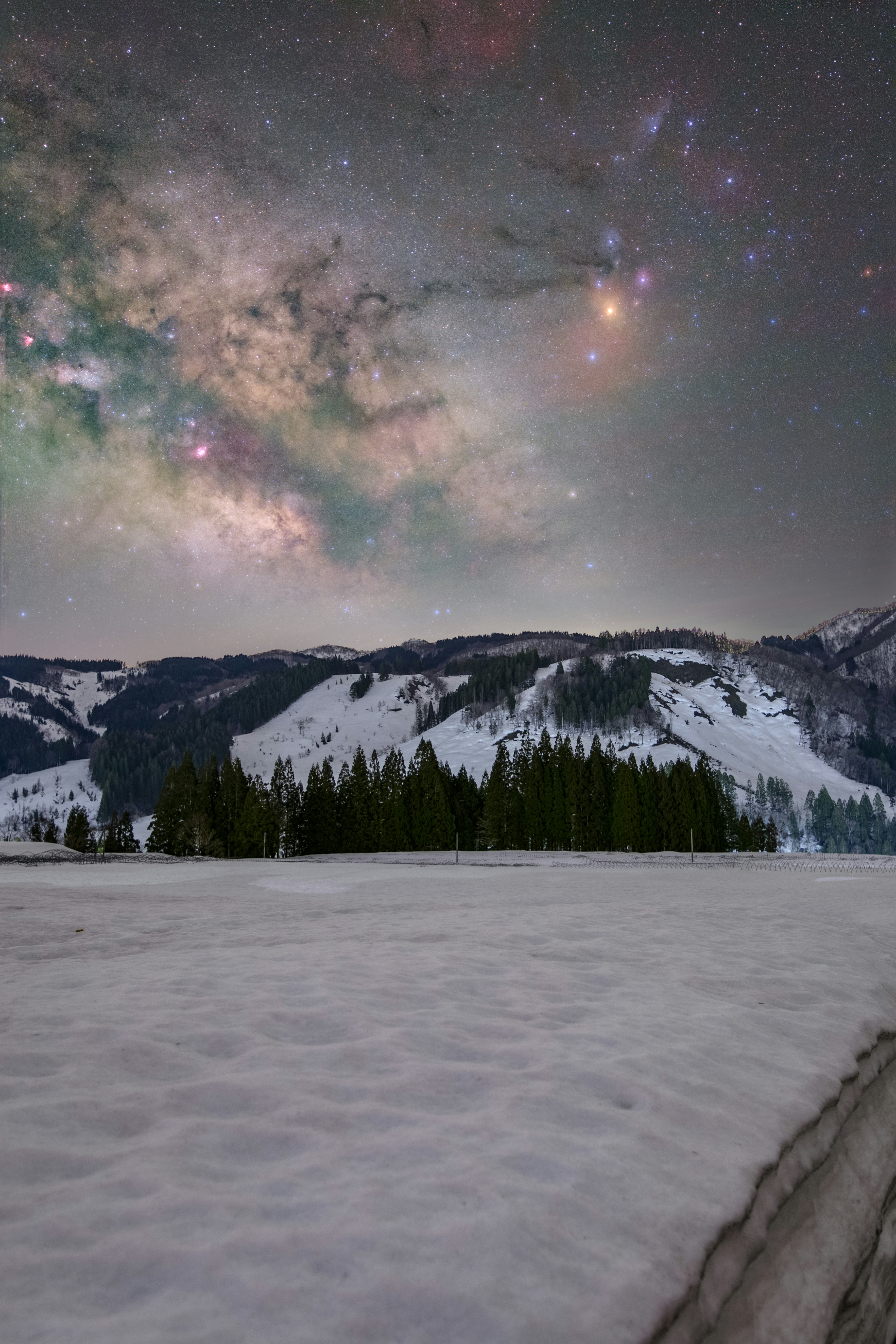 雪原と山並みの上に広がる天の川の星空