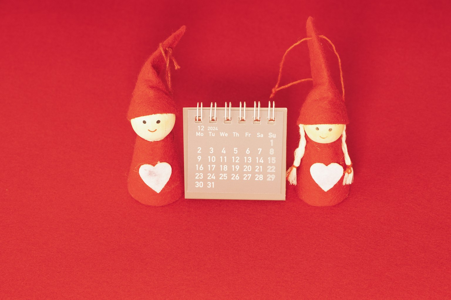 Dua boneka merah dengan hati dan kalender di latar belakang merah