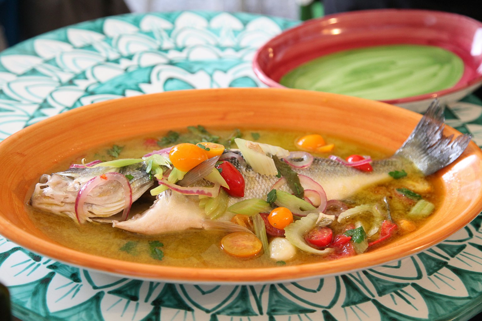 Eine lebendige Fischsuppe in einem orangefarbenen Teller auf einem grünen Tischdecken serviert