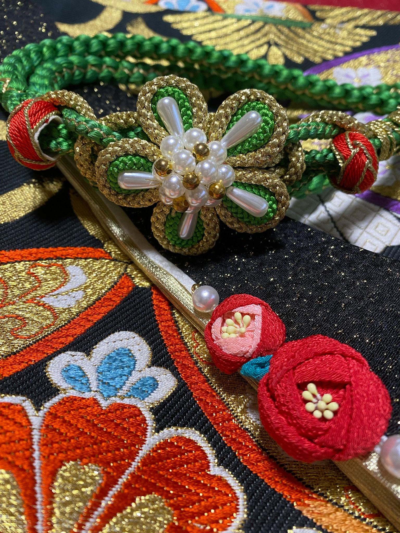 Traditional Japanese accessory with green braided cord and white flower decoration on embroidered fabric