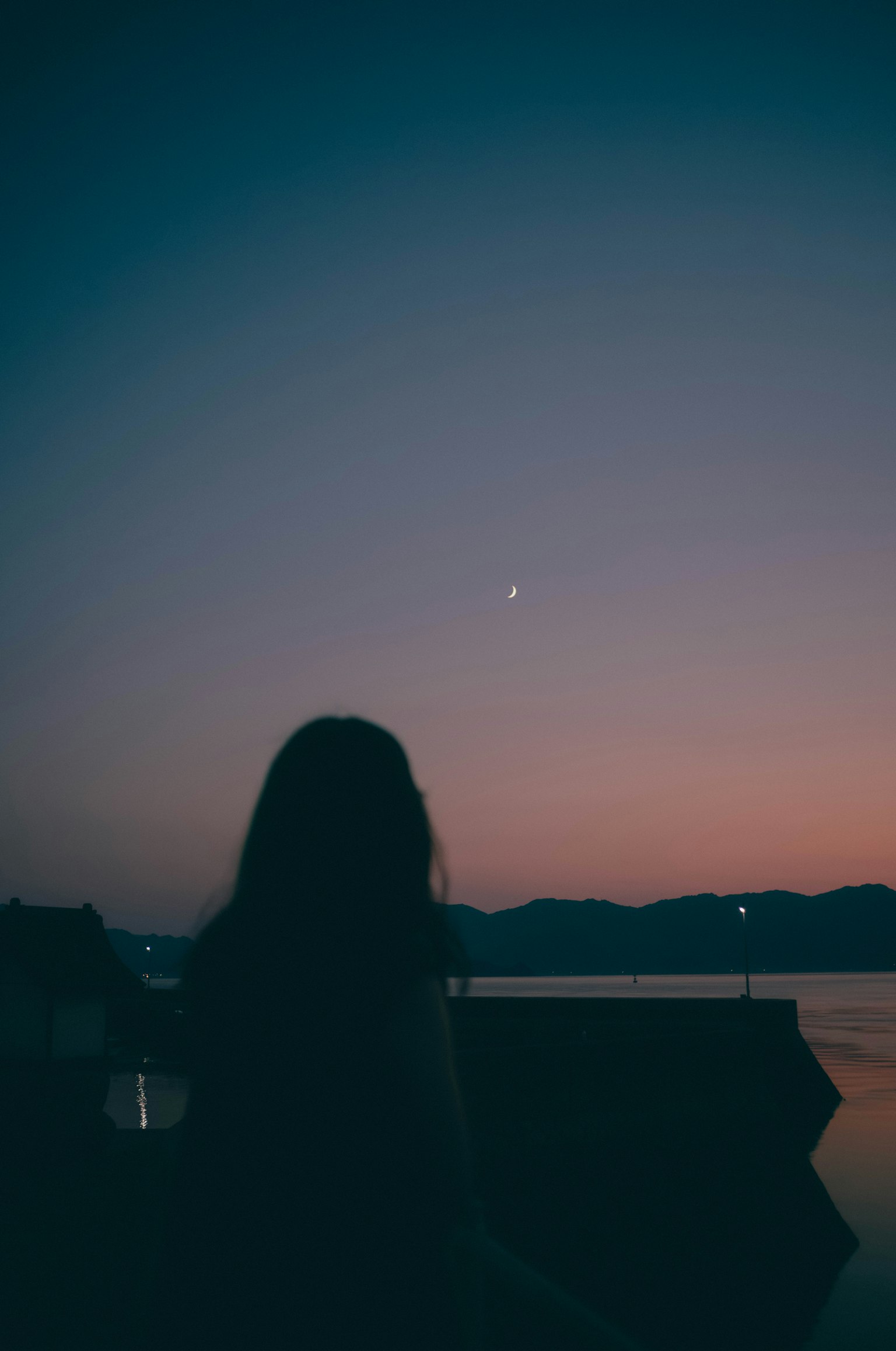 Siluet wanita berdiri di tepi danau saat senja Bintang berkelap-kelip di langit malam