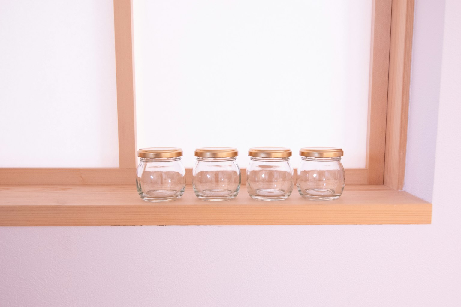 Bocaux en verre transparent avec des couvercles dorés alignés sur un rebord de fenêtre en bois