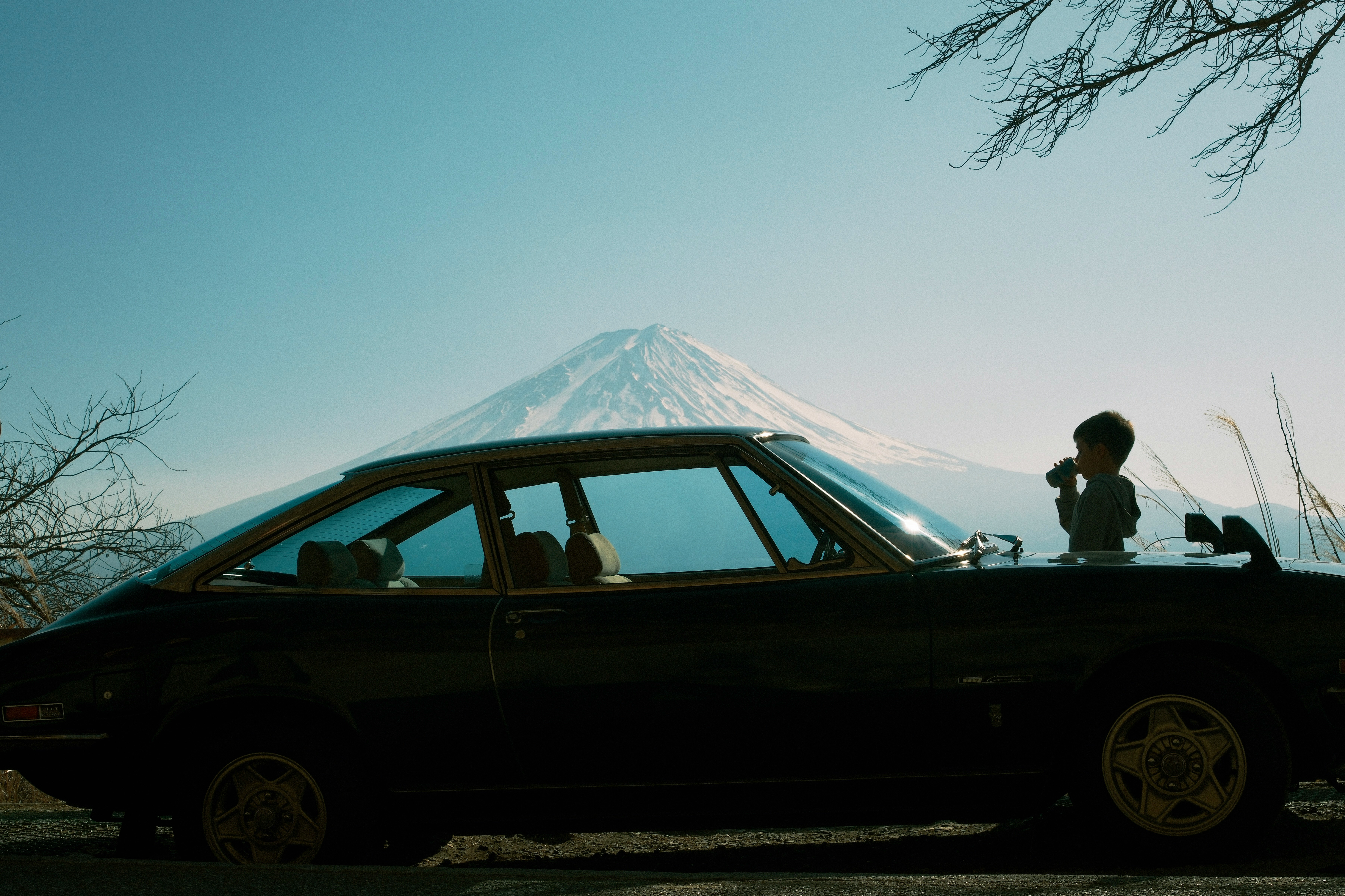 Silhouette seseorang di dekat mobil yang terparkir di tepi danau, menatap Gunung Fuji