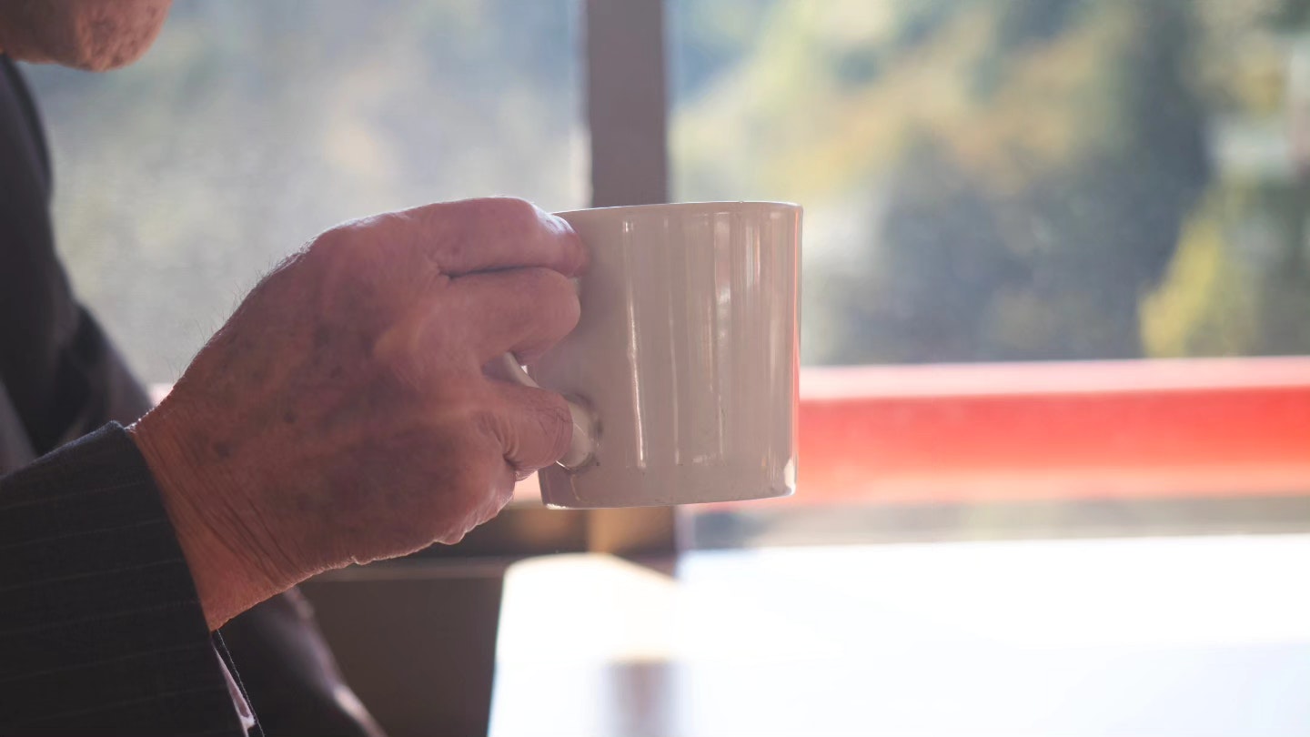 Primo piano di una mano che tiene una tazza vicino a una finestra