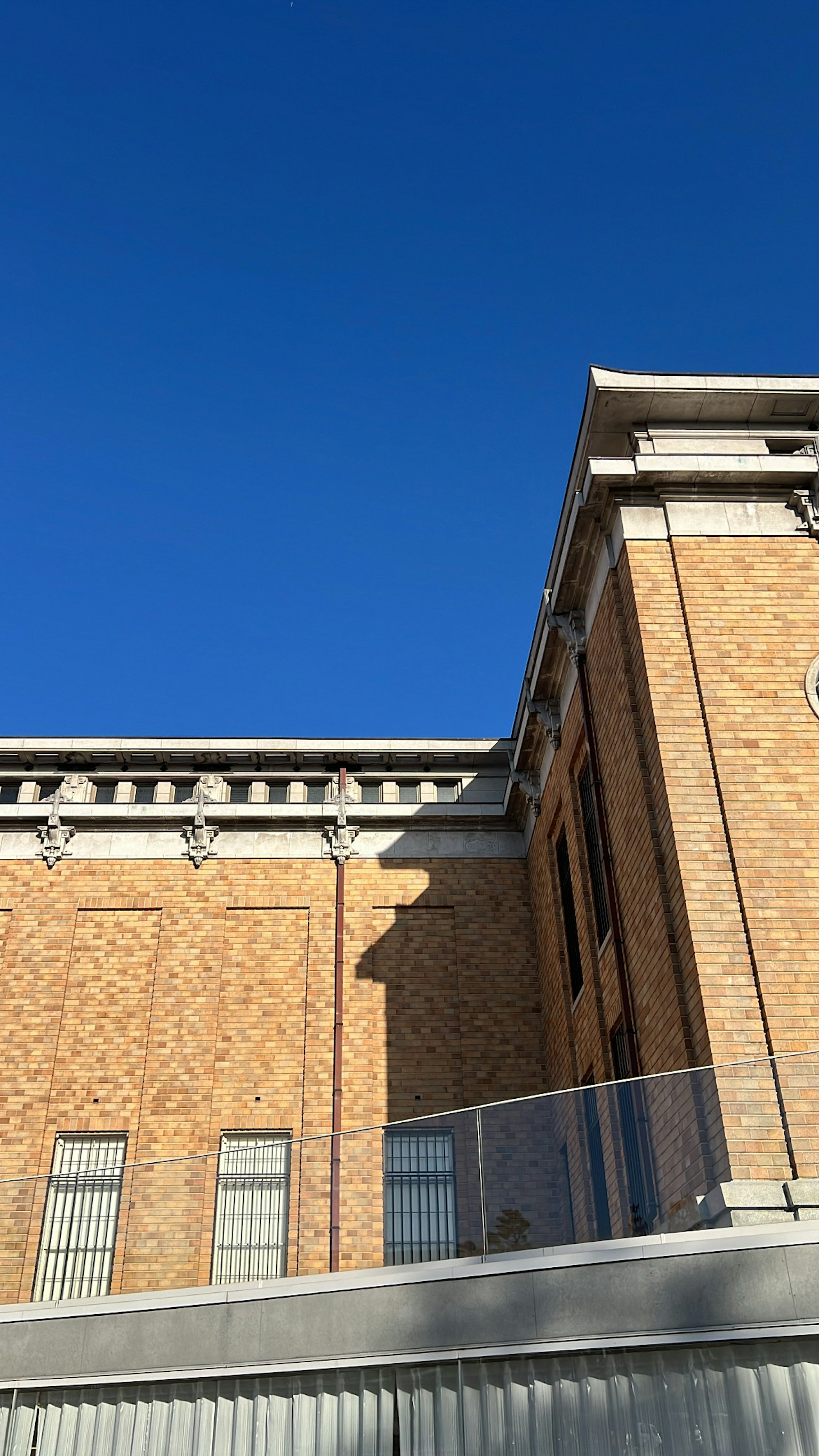 Part of a brick building under a clear blue sky with shadows