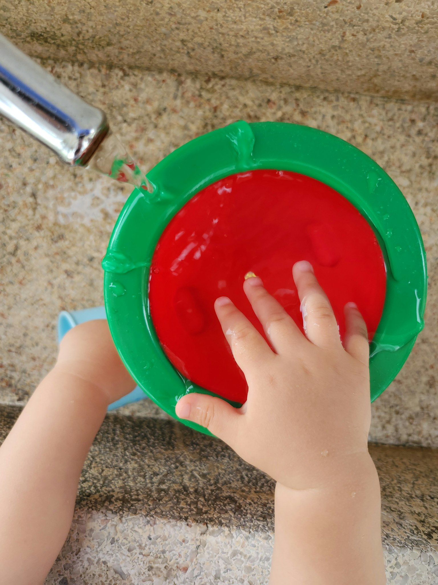 Tangan anak menyentuh cairan merah dalam mangkuk hijau