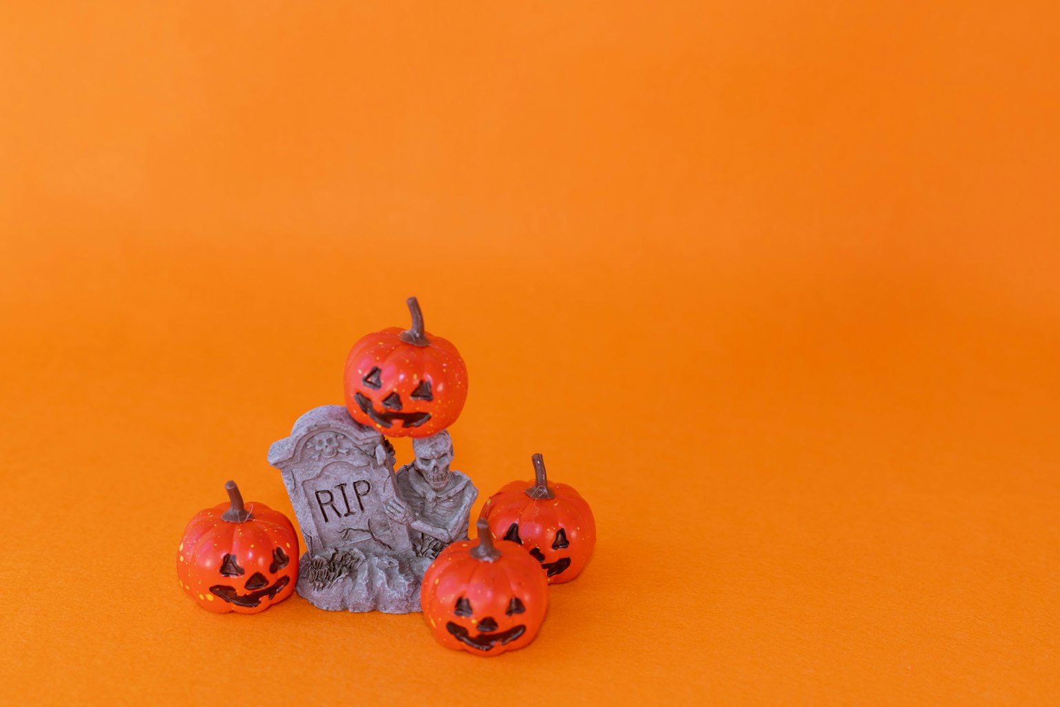 Cinco calabazas Jack-o'-lantern y una decoración de lápida sobre un fondo naranja
