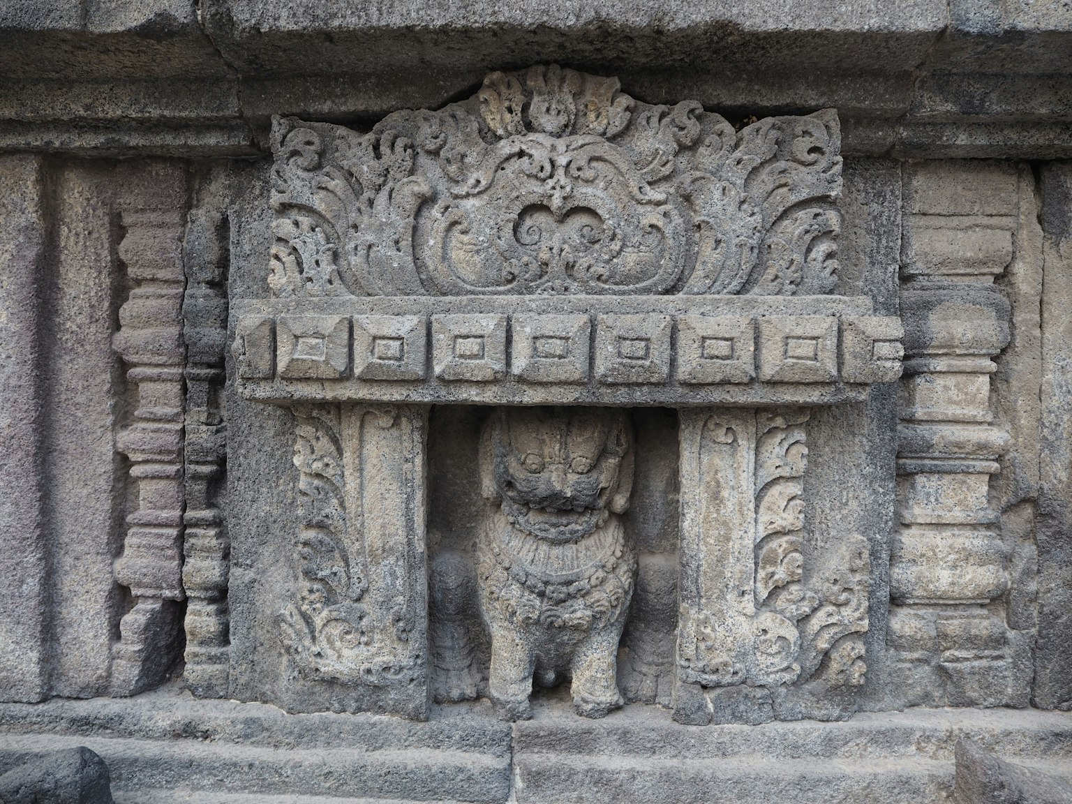 Sezione di muro di un antico tempio con intricate sculture in pietra e una statua di leone