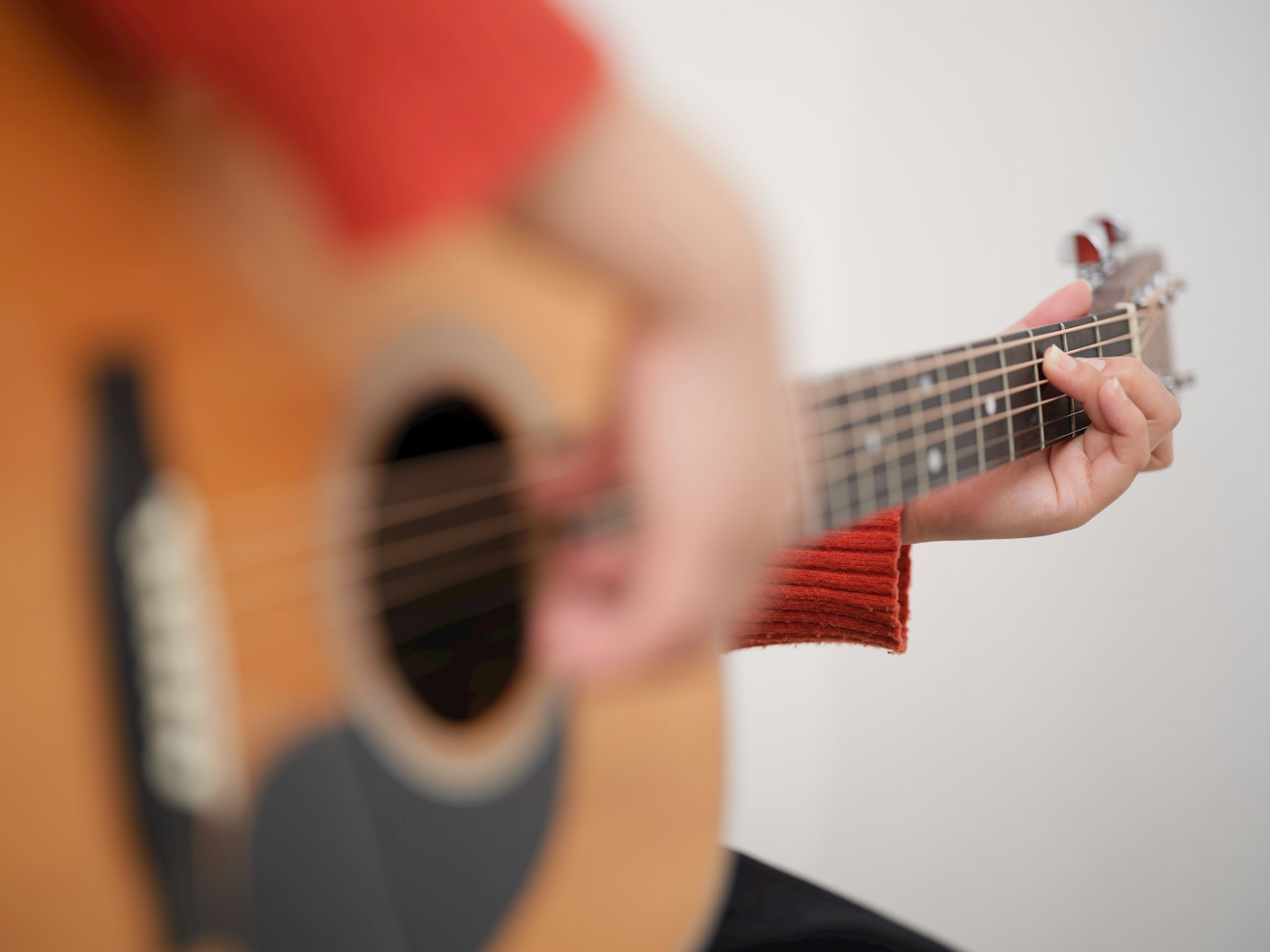 Close-up tangan yang memainkan gitar akustik mengenakan sweter merah