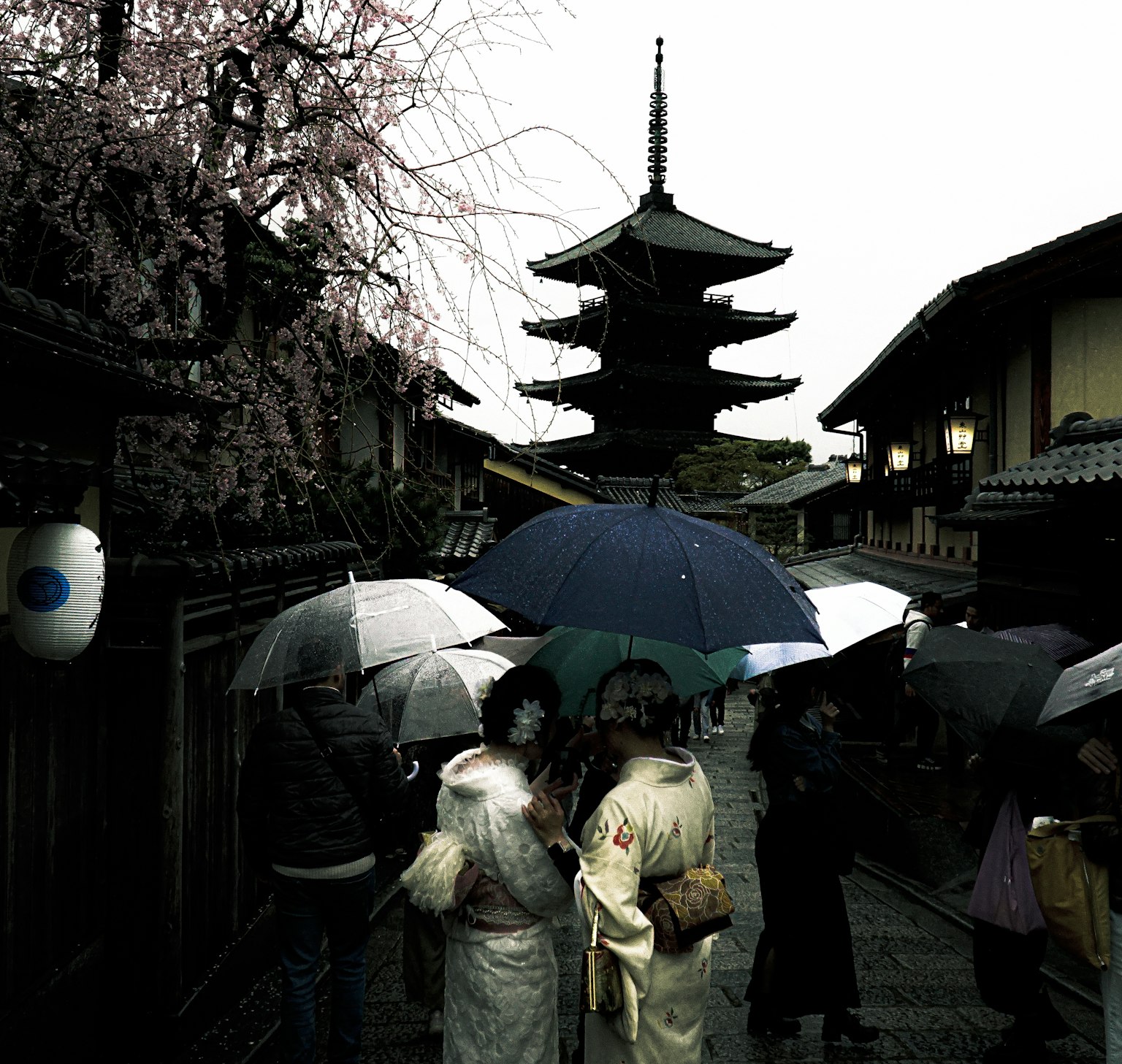 People in kimonos holding umbrellas with a pagoda in the background in an old street