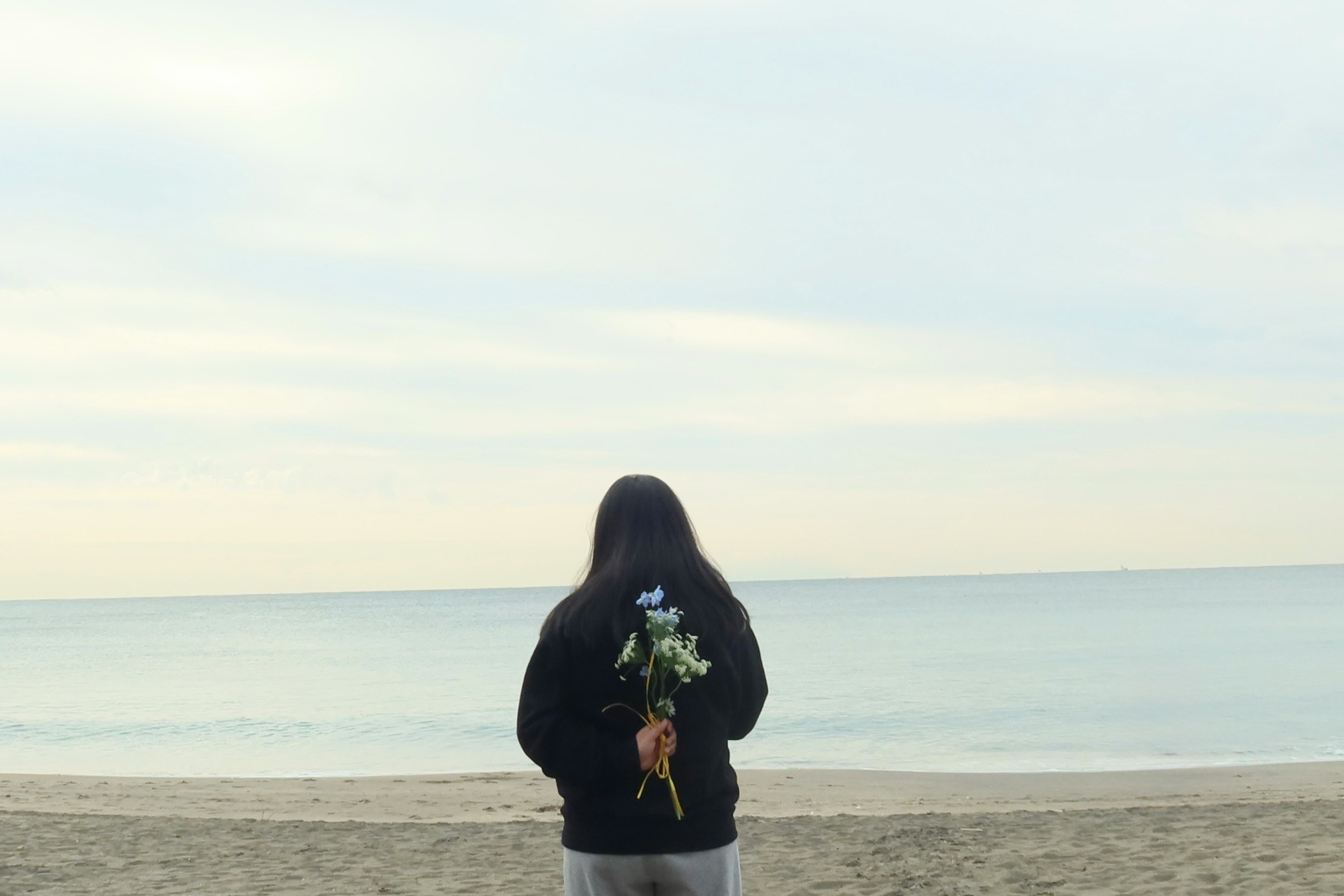 A lone traveler holding a bouquet on the beach