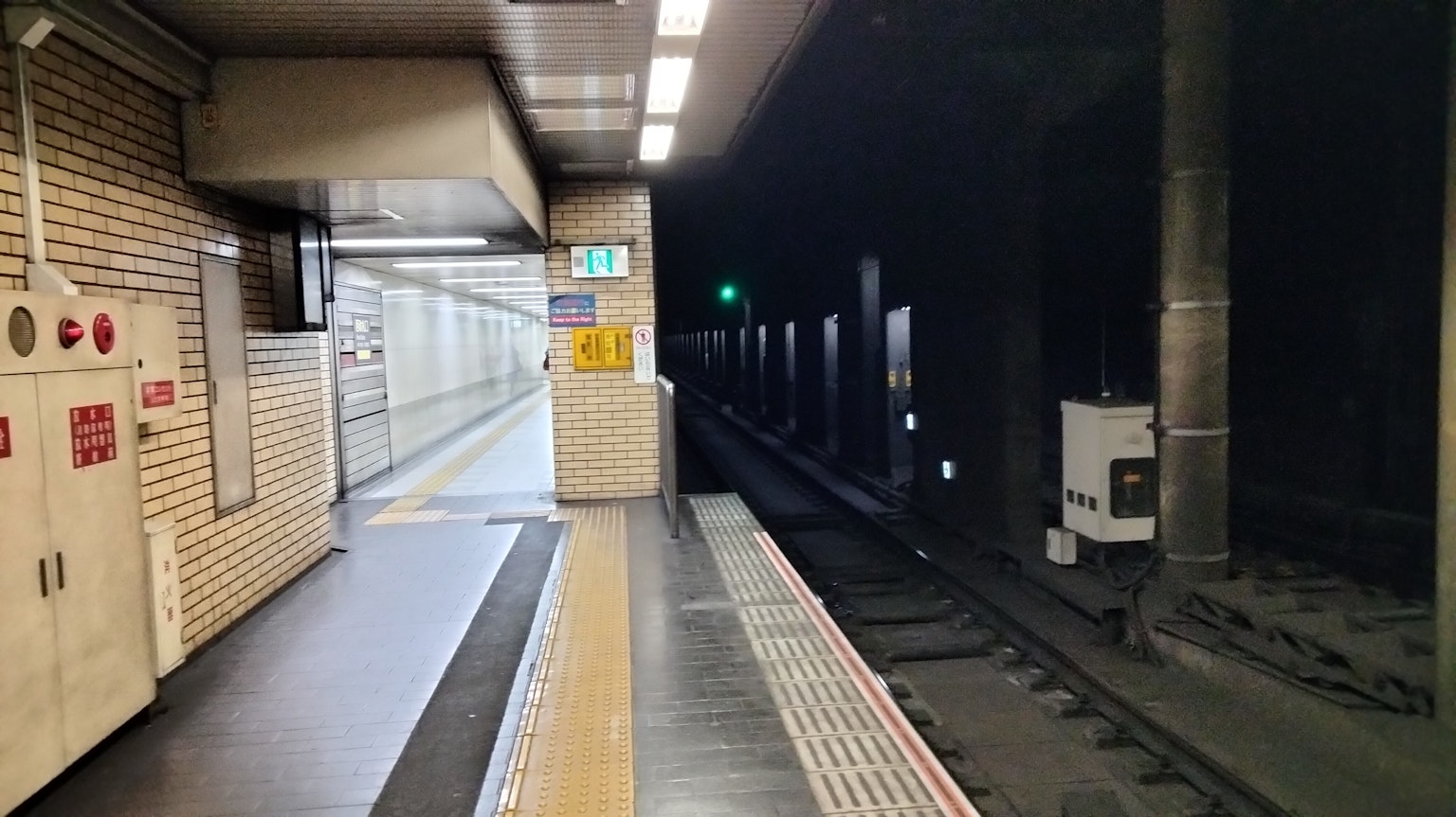 Plattform einer U-Bahn-Station mit einem grünen Signal in einem dunklen Tunnel
