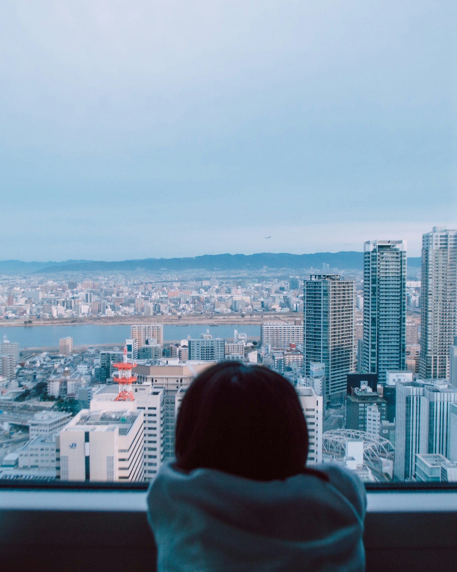 Anak melihat ke luar jendela ke pemandangan kota dengan gedung pencakar langit dan cakrawala yang jauh
