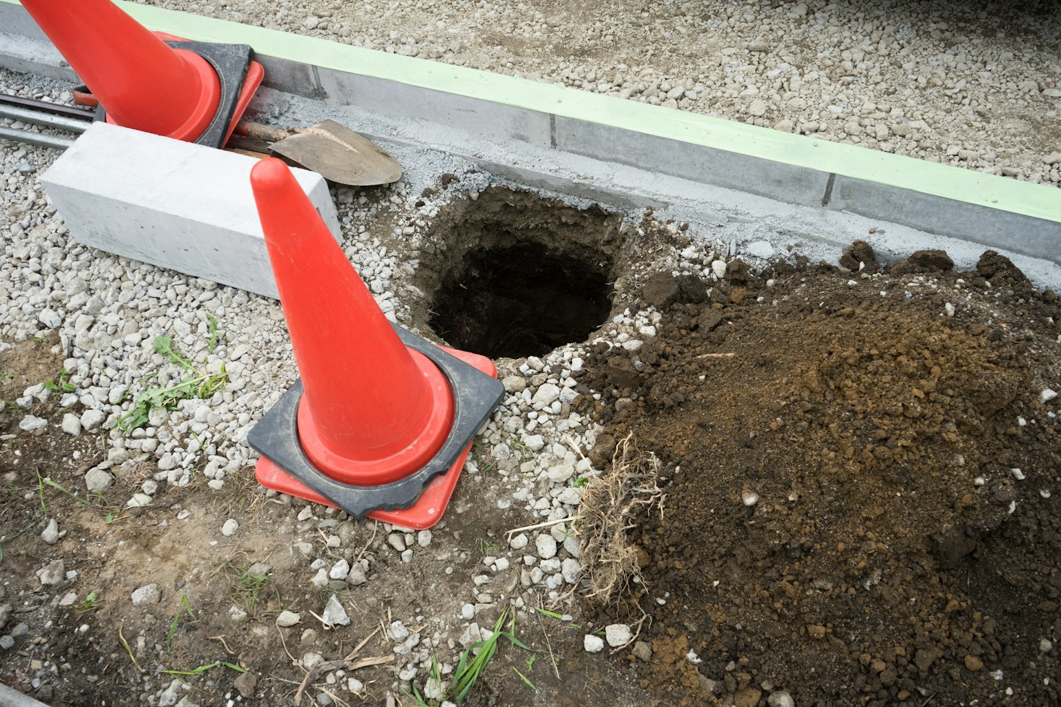 Baustelle mit einem Ausgrabungsloch und orangefarbenen Kegeln sowie Erde