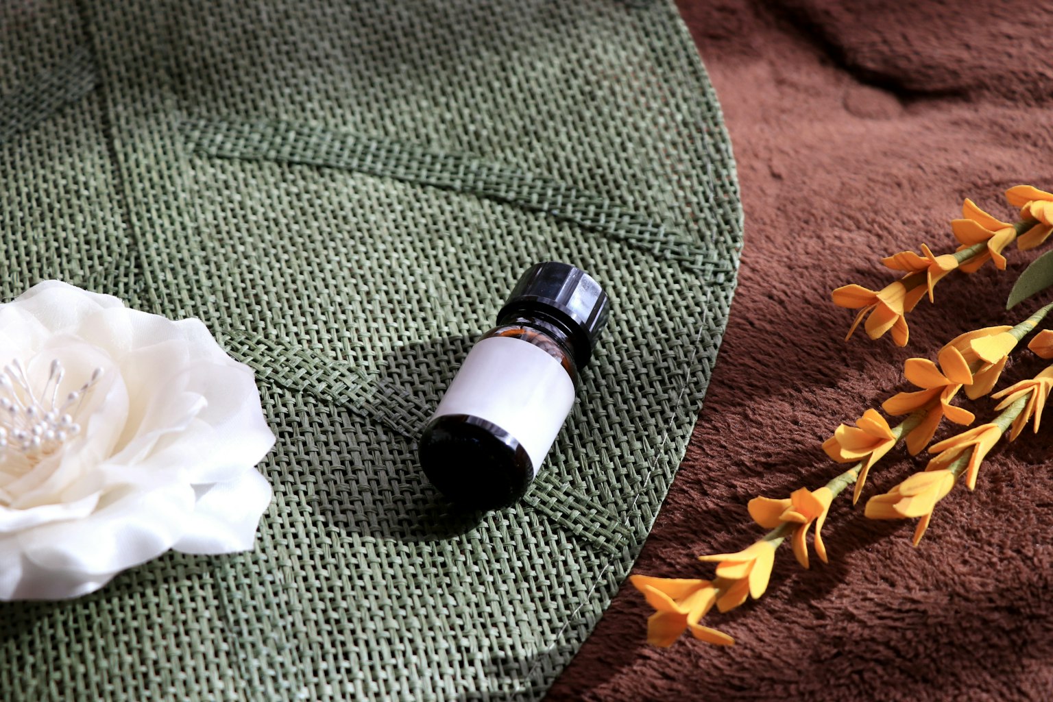 A white flower and an essential oil bottle placed on a green fabric